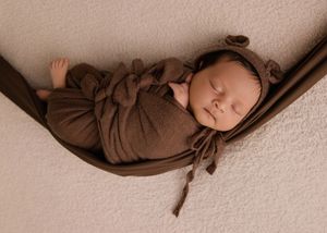 Newborn baby wrapped in soft brown fabric lying on beige textured backdrop in artistic photography composition.