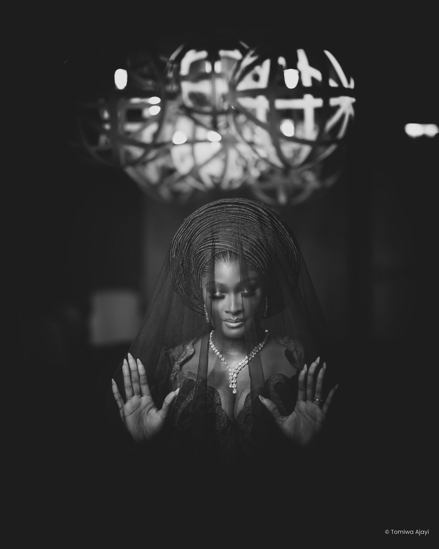A dramatic black and white portrait showing hands raised in a contemplative pose against a dark background.