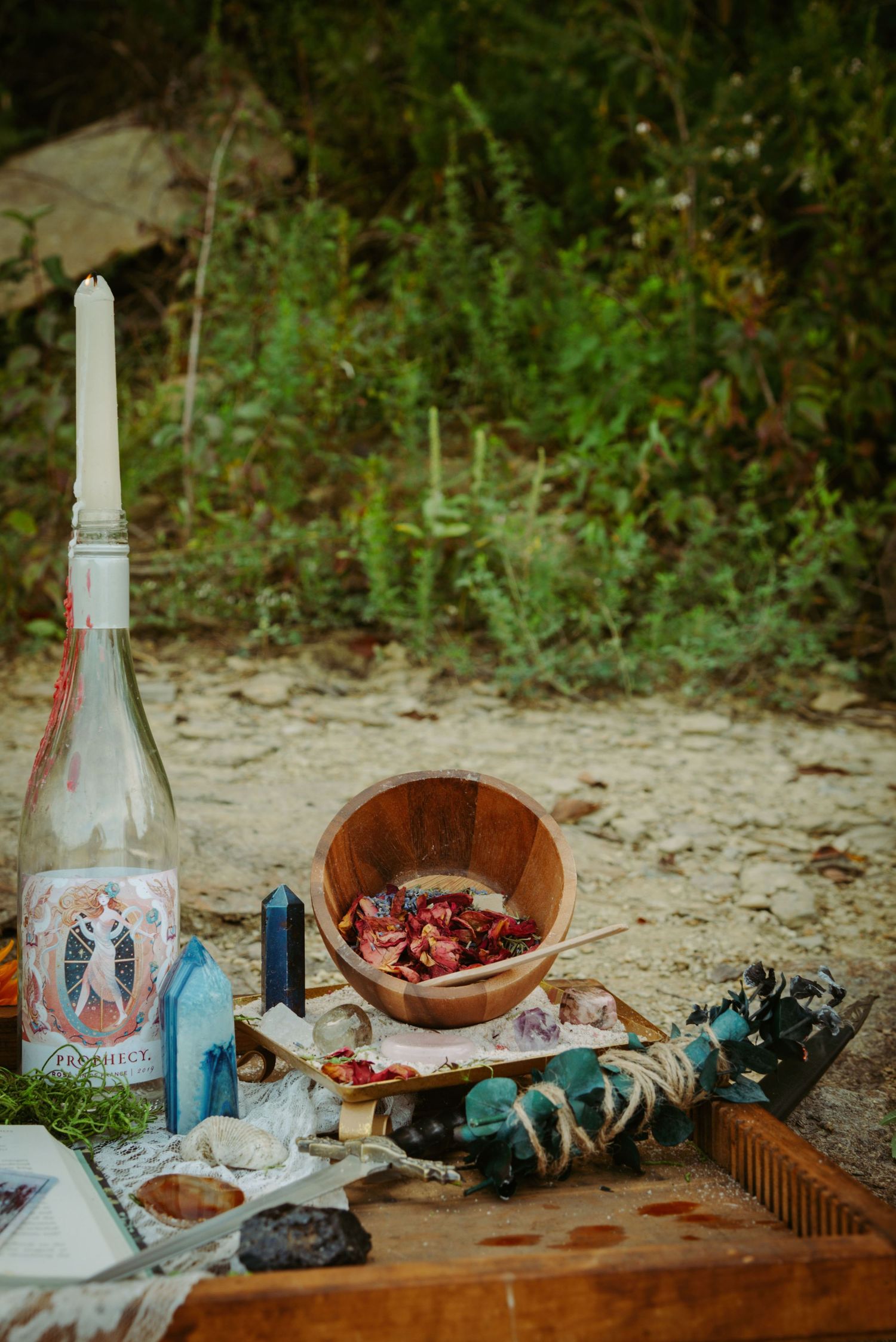 A rustic outdoor table setting with glass bottles, wooden bowls, and scattered items on a sandy surface.