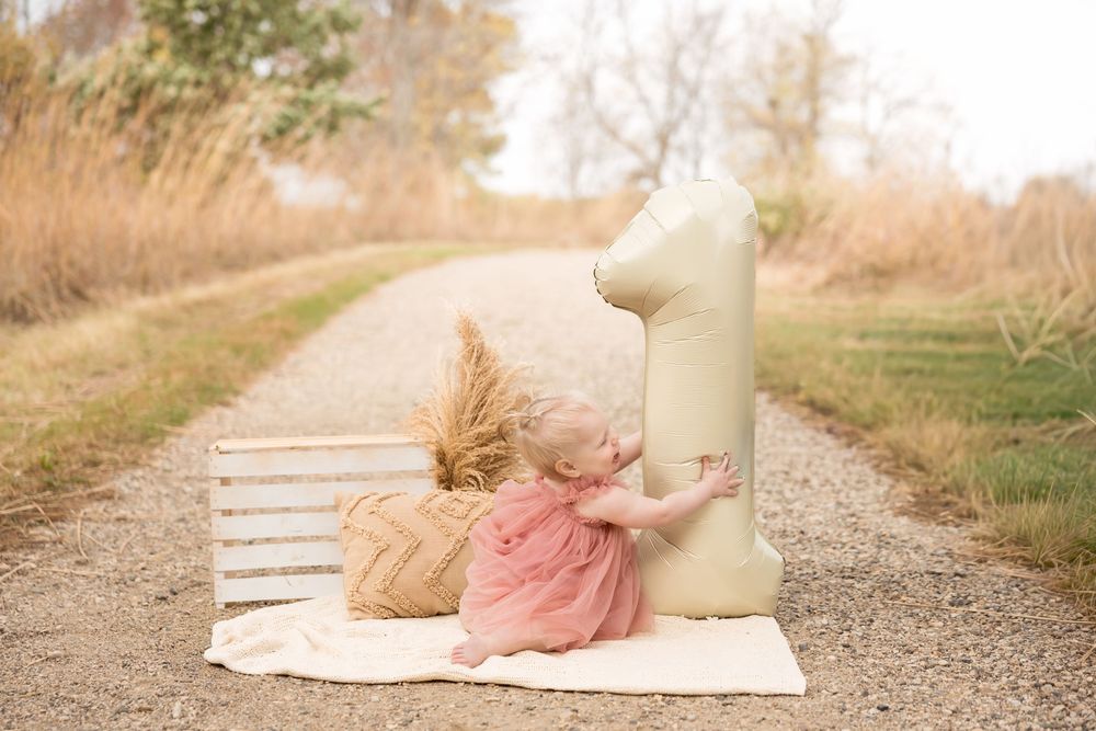 Pink tulle dress and decorative number one setup for first birthday photoshoot on outdoor path with pampas grass.