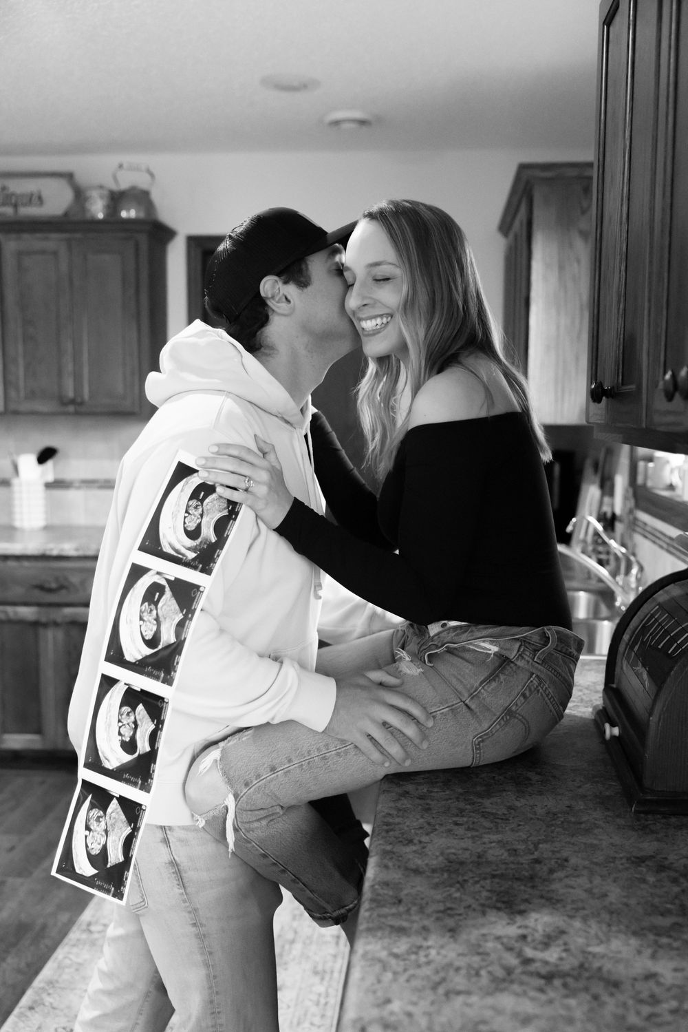 Couple sharing an intimate moment while looking at ultrasound photos in a kitchen.