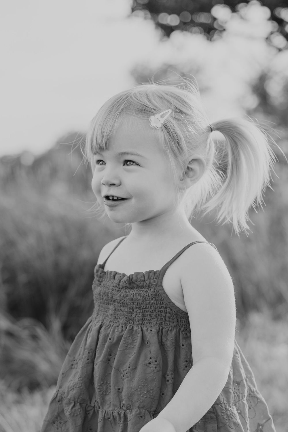 Black and white portrait of young child with pigtails smiling outdoors.