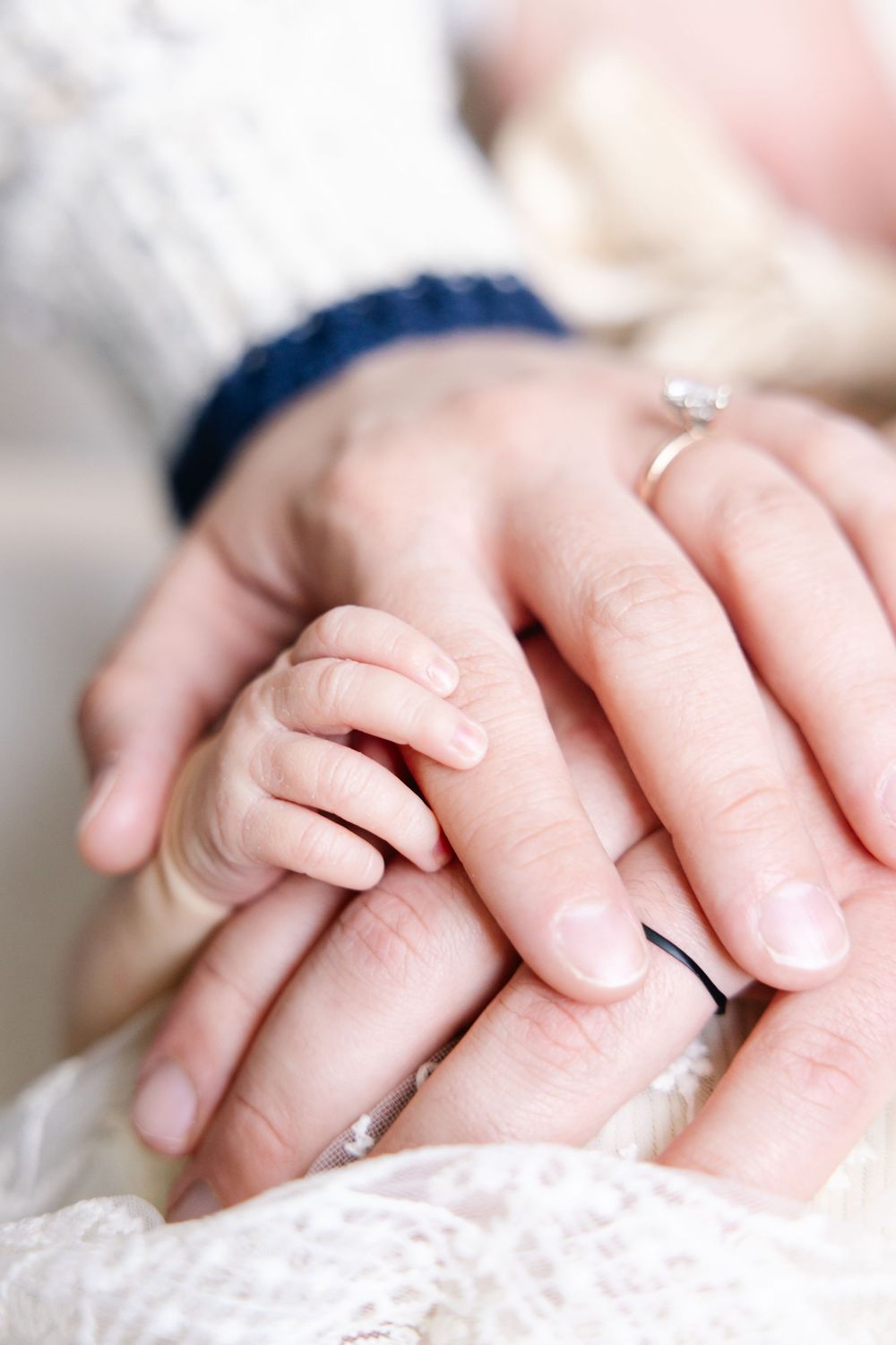 Gentle close-up of hands touching with a wedding ring visible on soft white fabric.