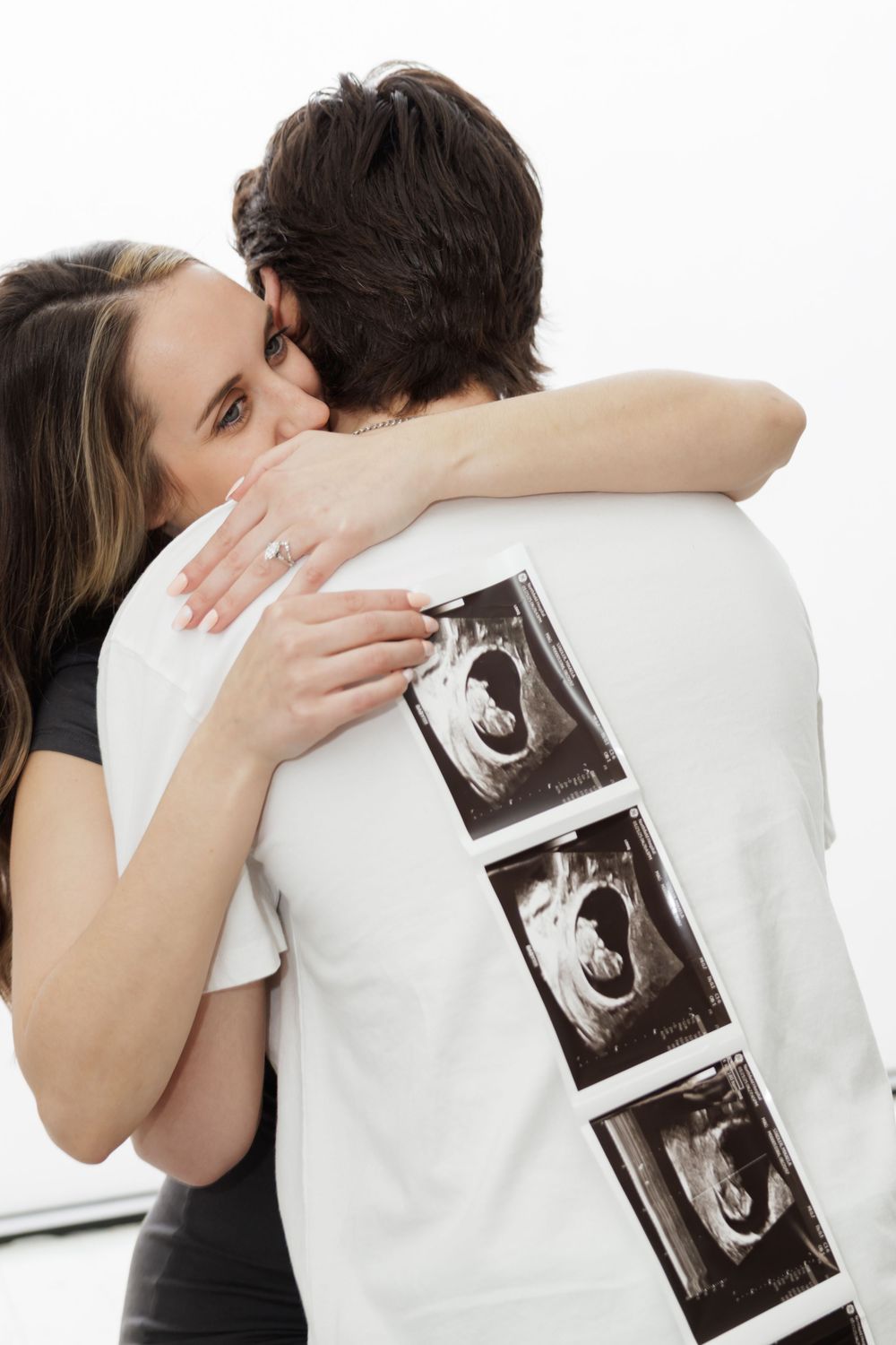 Couple embracing while holding ultrasound photos against white background.