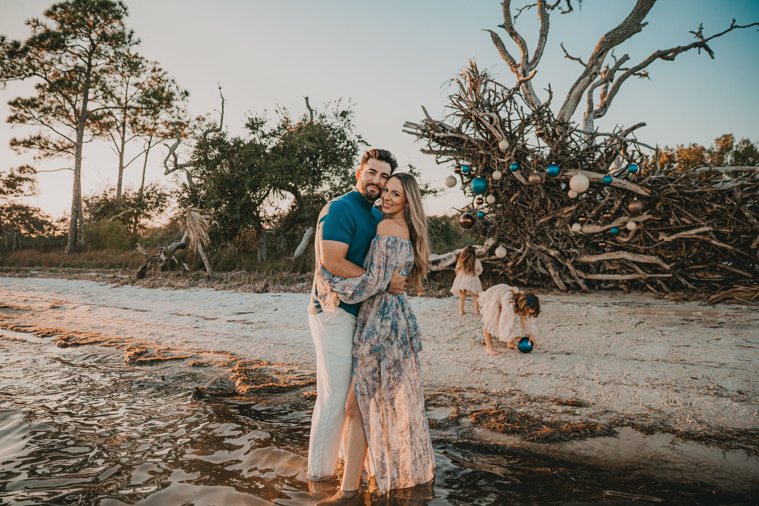 A beachside photoshoot at sunset with fallen trees and driftwood creating a natural backdrop on the sandy shore.