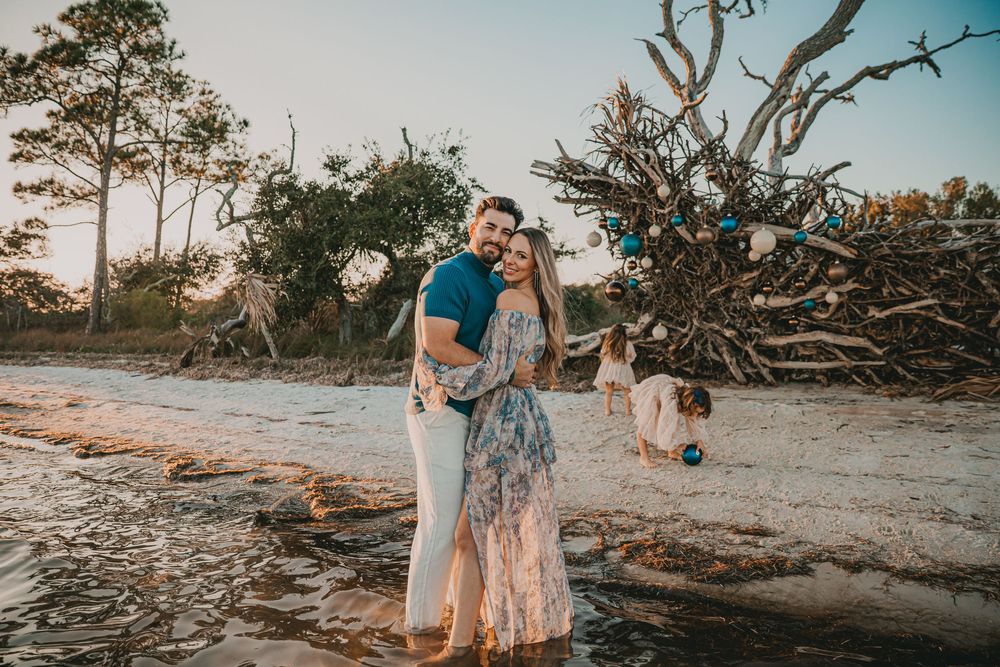 A beachside photoshoot at sunset with fallen trees and driftwood creating a natural backdrop on the sandy shore.