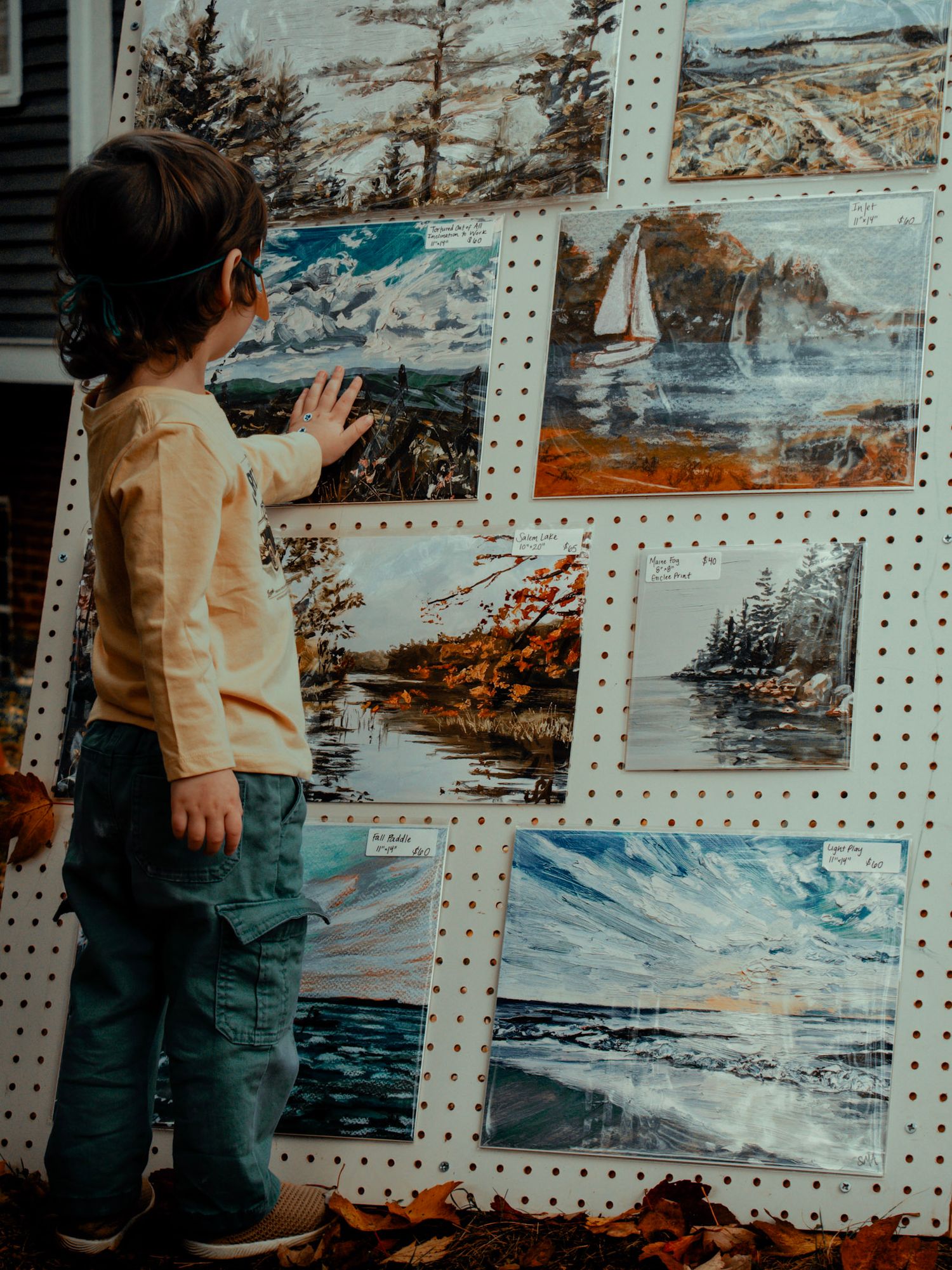 Pegboard wall display featuring coastal landscape artwork and nautical scenes.