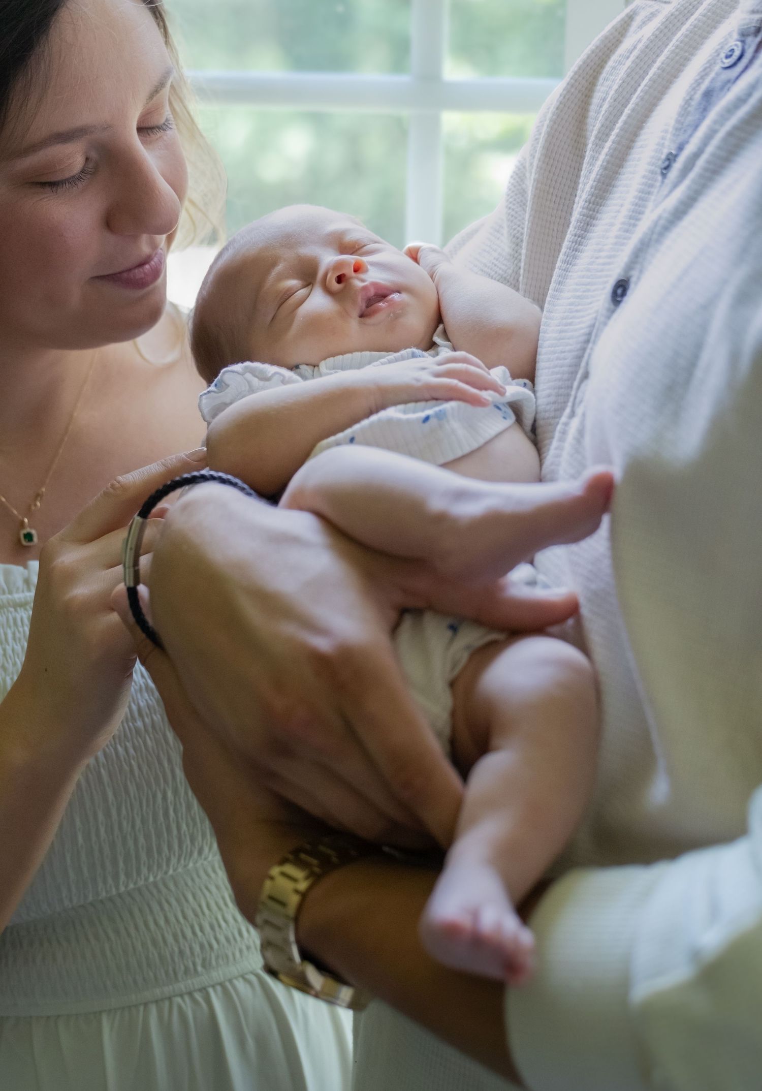 Newborn baby sleeping peacefully in parents' arms by a sunlit window.