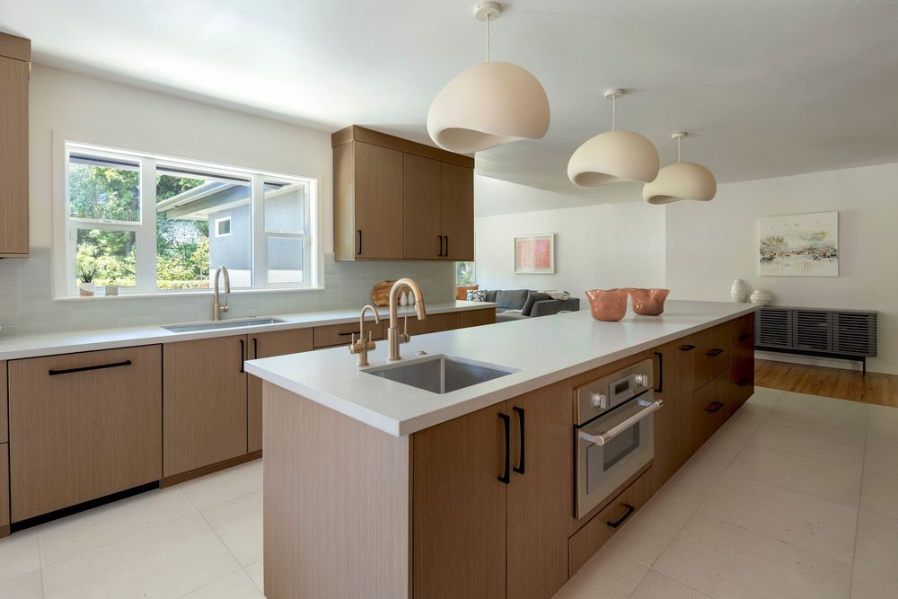 Modern kitchen with brown cabinets, white countertops, dual sinks, stainless steel oven, and pendant lights over island.