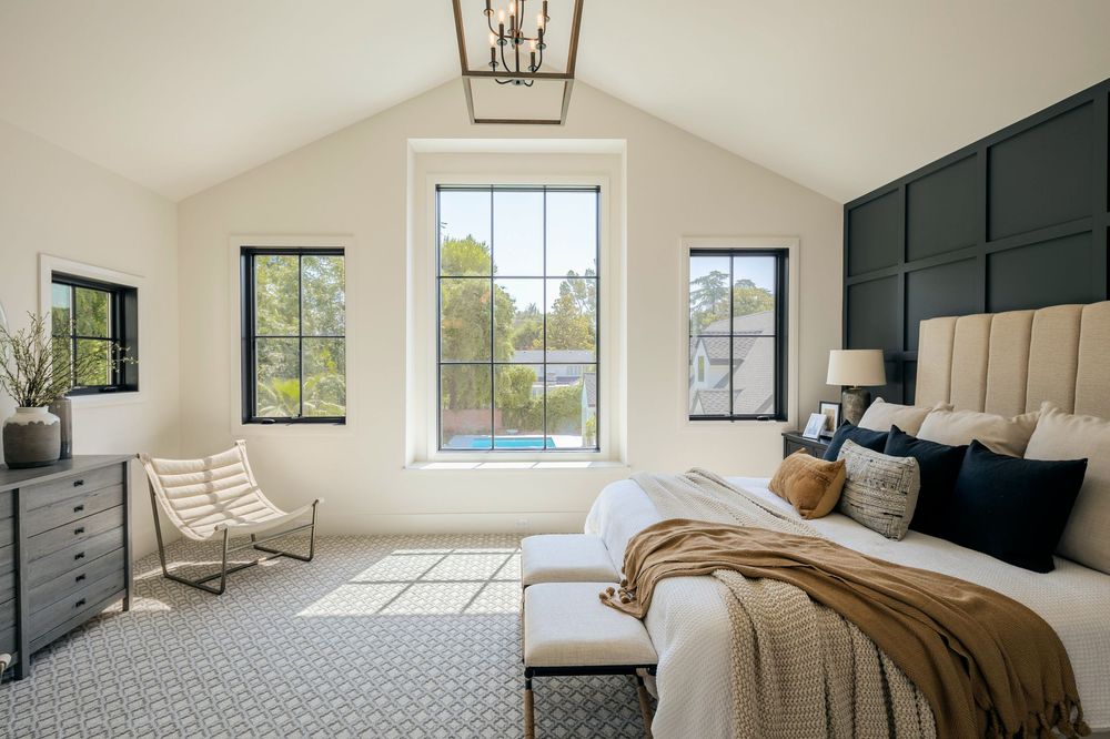 Modern bedroom interior with gray upholstered headboard, white bedding, and natural light from windows.