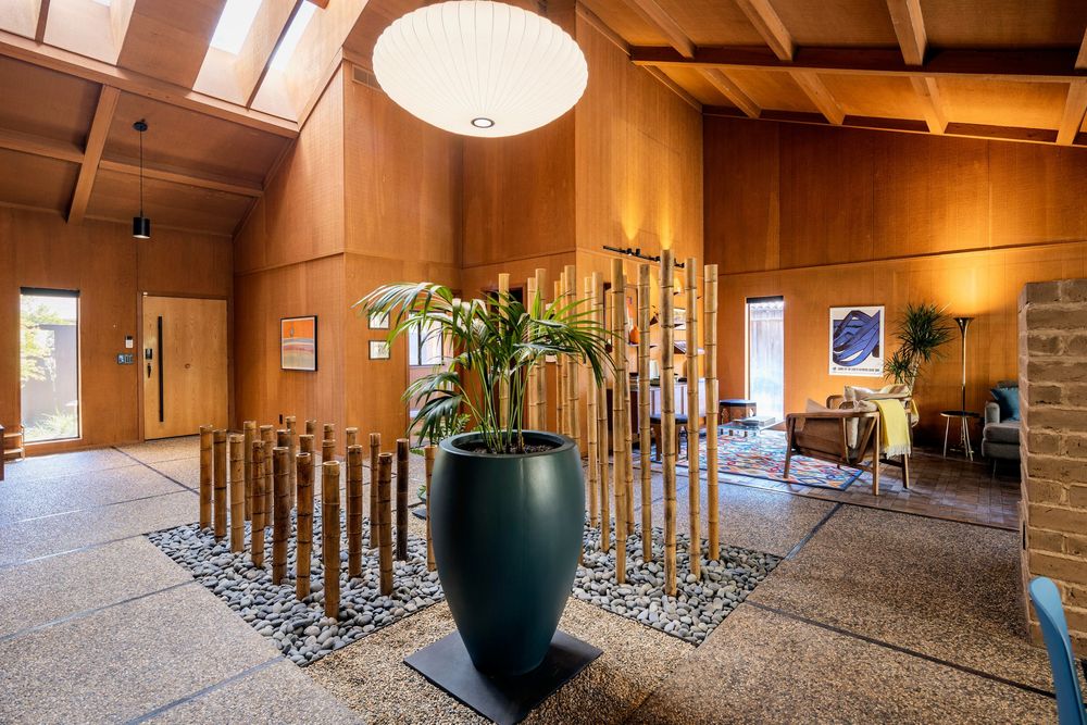 Modern hotel lobby interior with wooden beams, chandelier lighting, and large black decorative planters.
