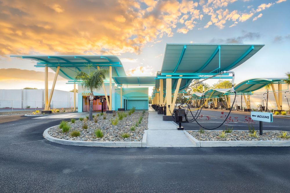 Modern teal-roofed commercial building with tropical landscaping at sunset, featuring covered walkways and vibrant sky.