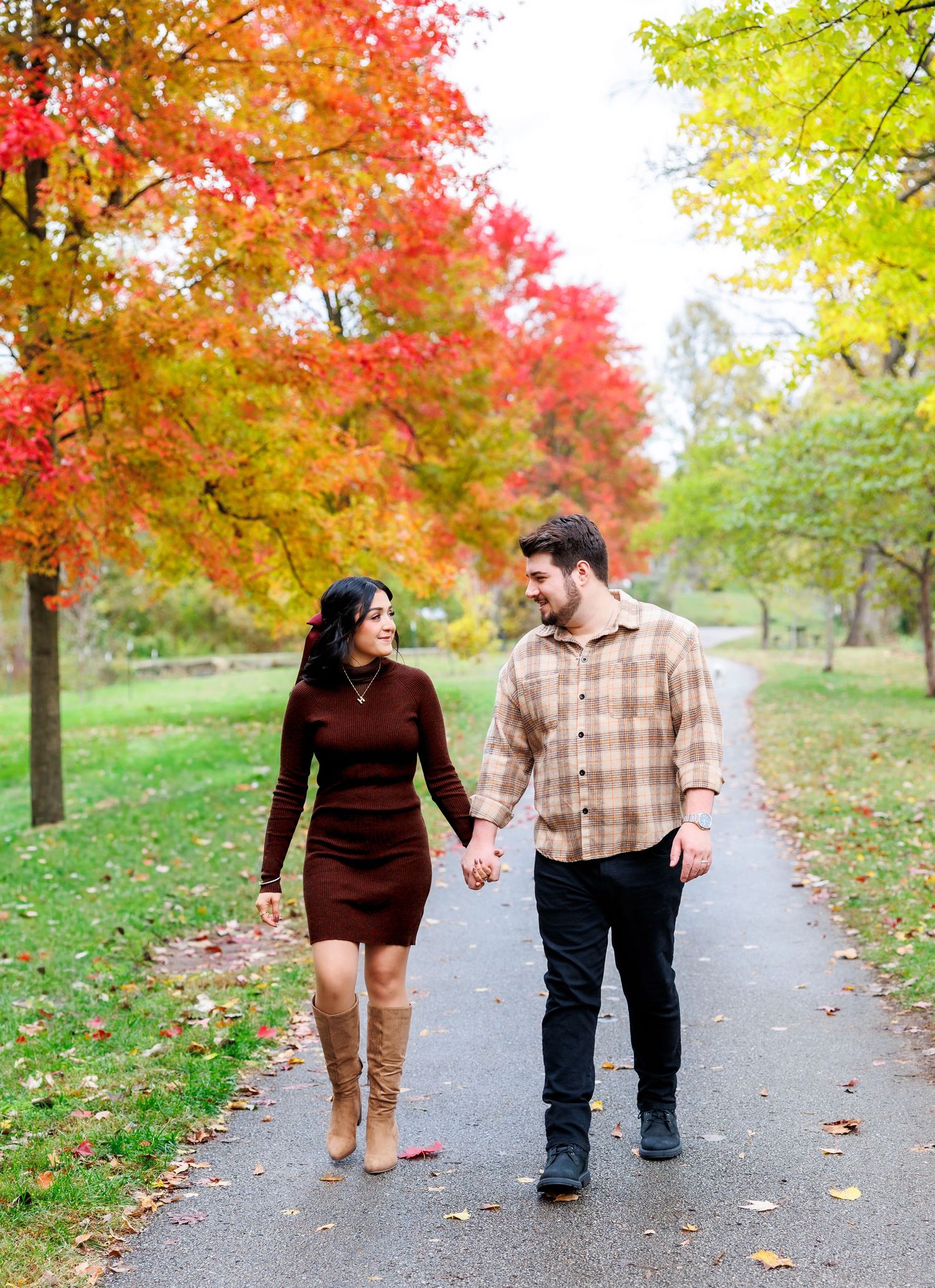 A couple stands together on a wooden dock overlooking a serene lake with autumn trees and boat docks in the background.