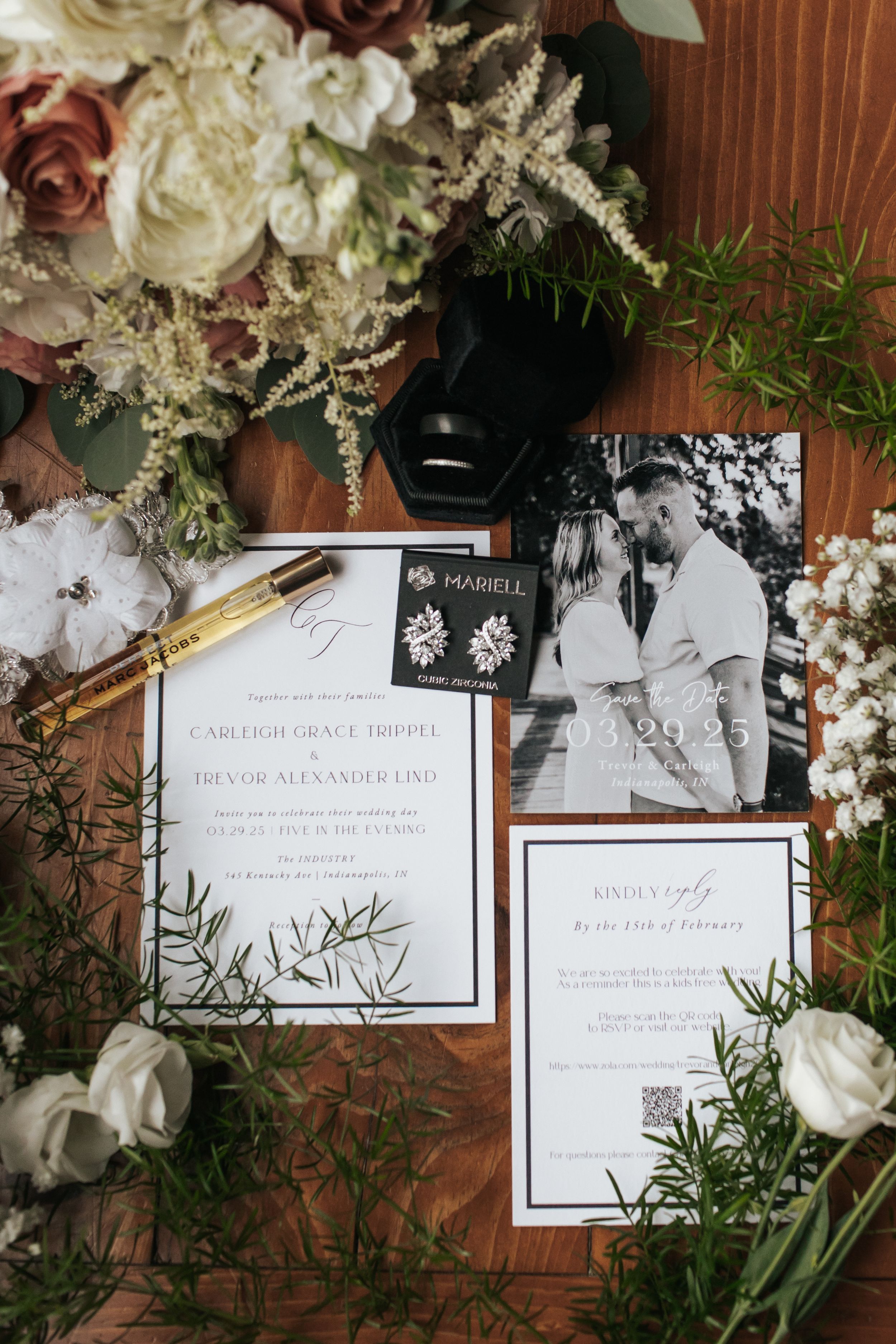 Elegant wedding invitation suite with white floral arrangements and greenery displayed on wooden surface.