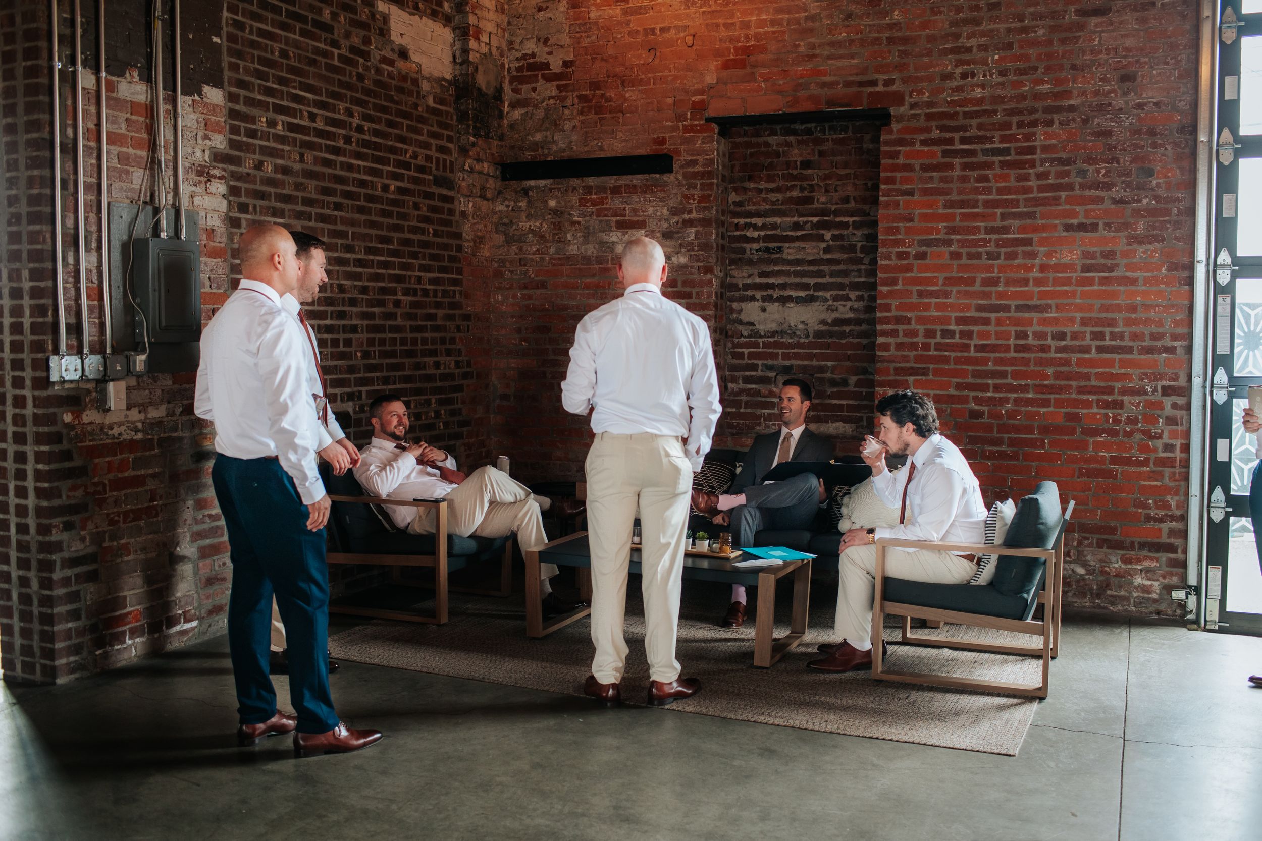 People in white protective suits gather in a brick-walled industrial space during an art installation or event.