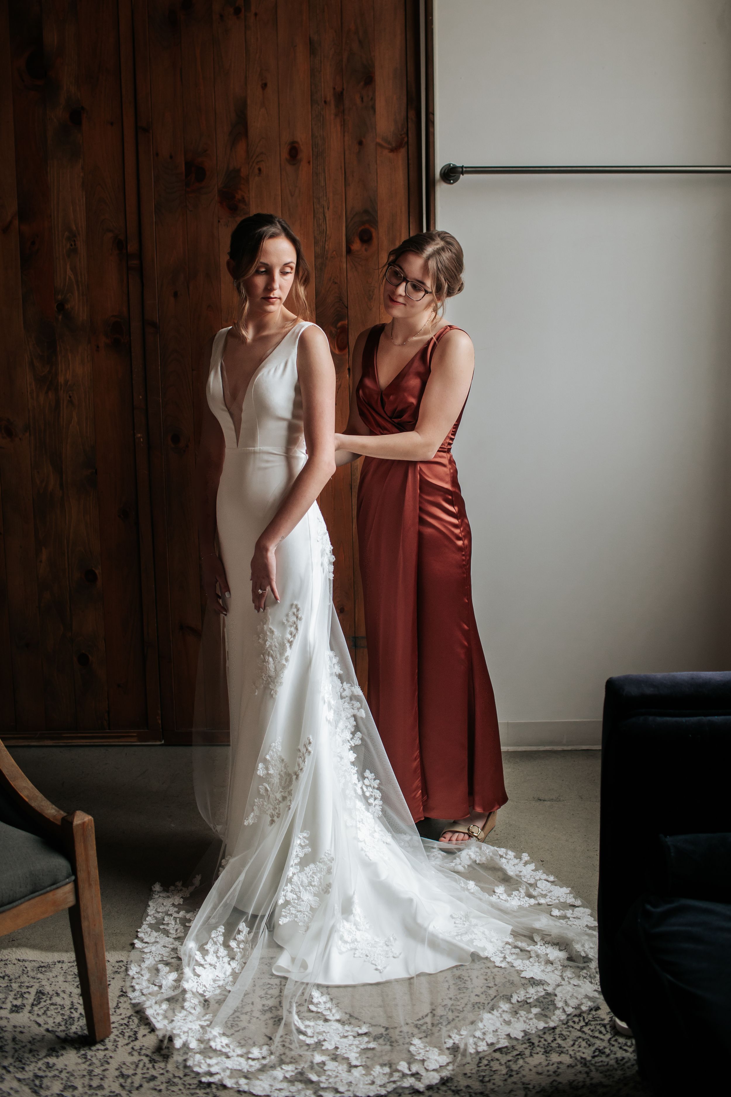 A wedding dress fitting scene shows a white gown with intricate lace details and a flowing train against wooden paneling.