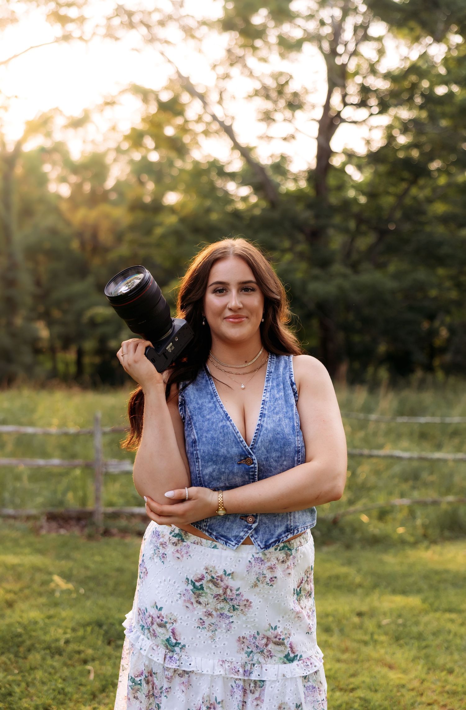 A photographer poses with professional camera equipment in a rustic outdoor setting.