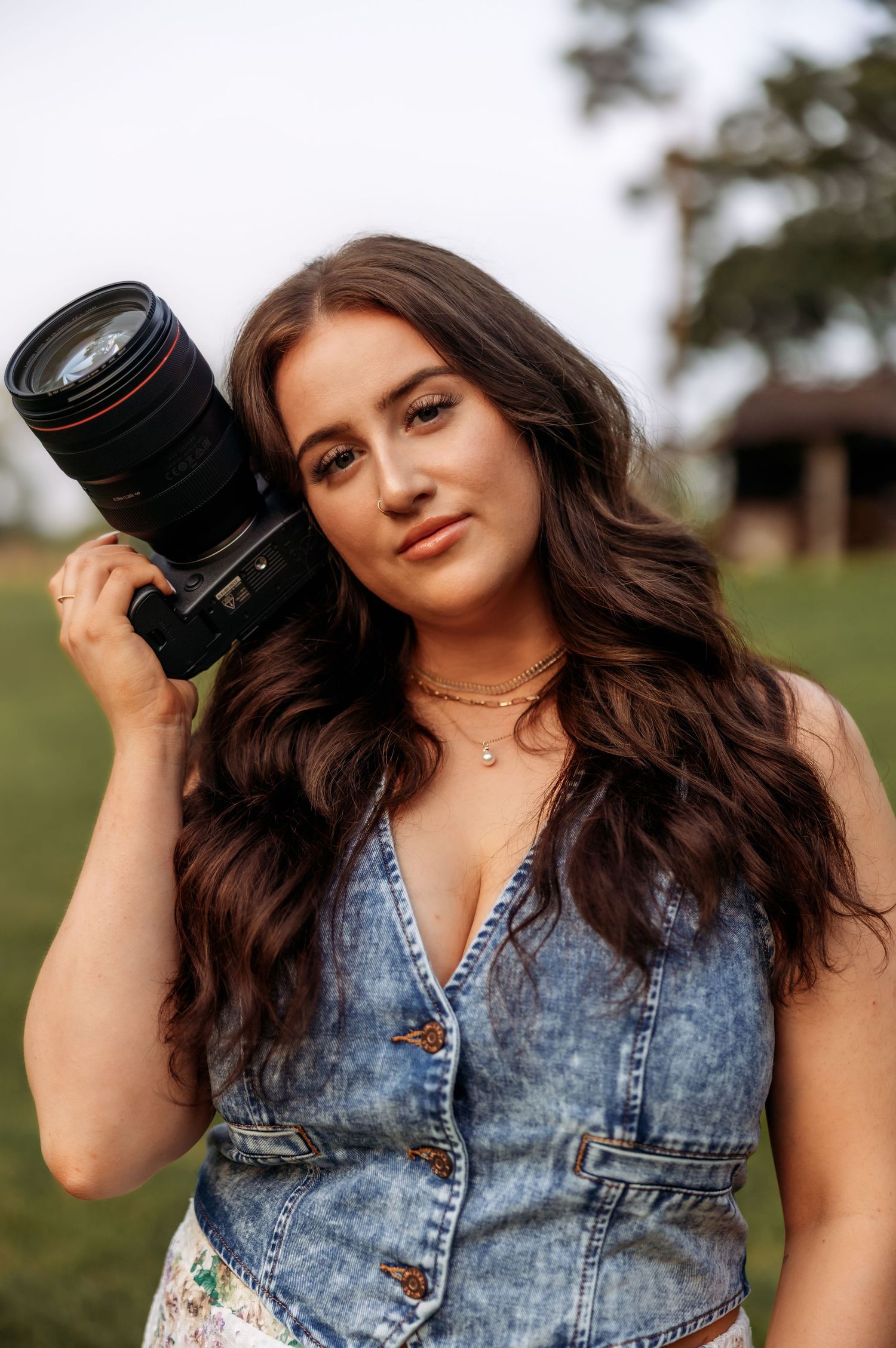 A photographer displays professional camera equipment while wearing denim and floral attire.