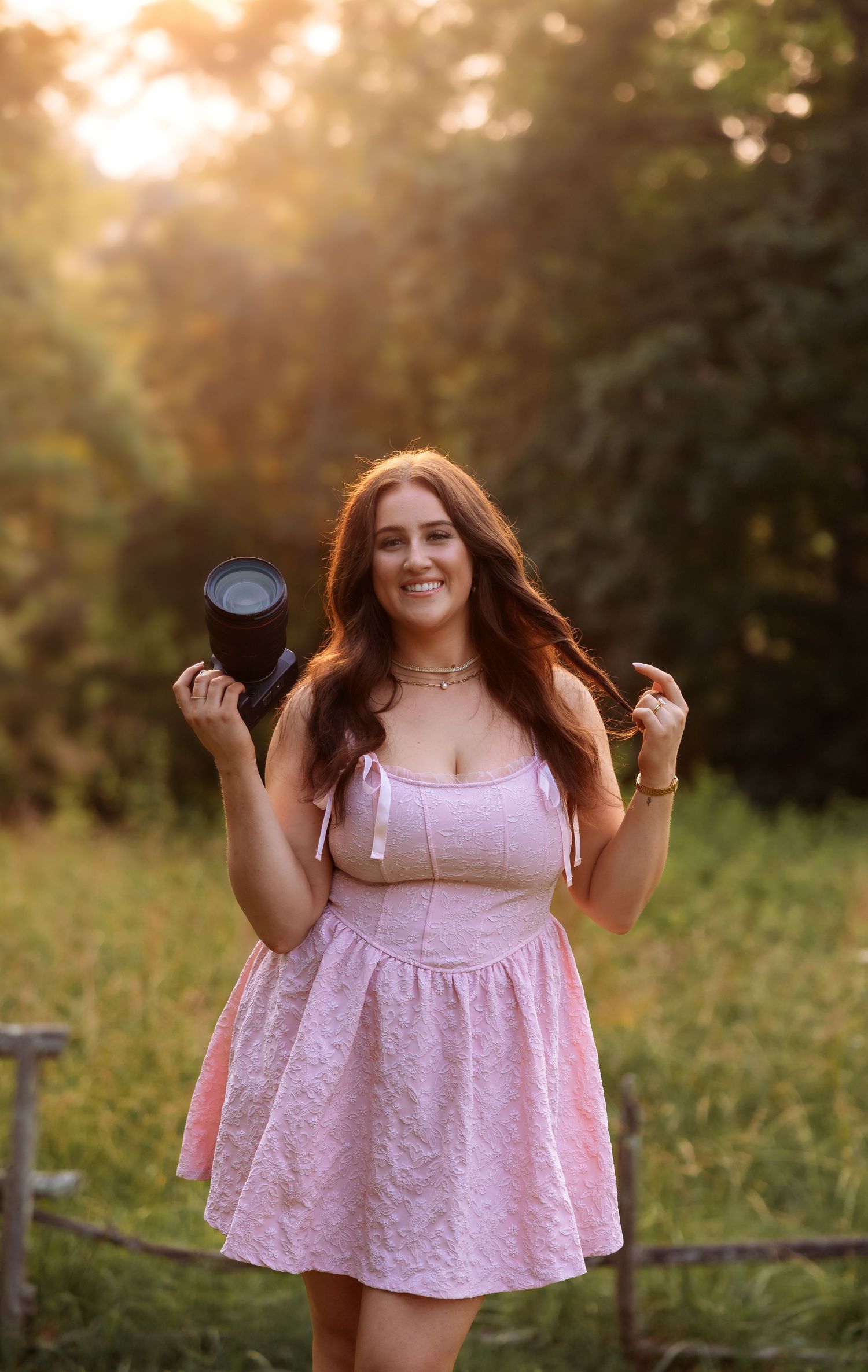 A person wearing a pink dress dances joyfully in a grassy field during sunset.