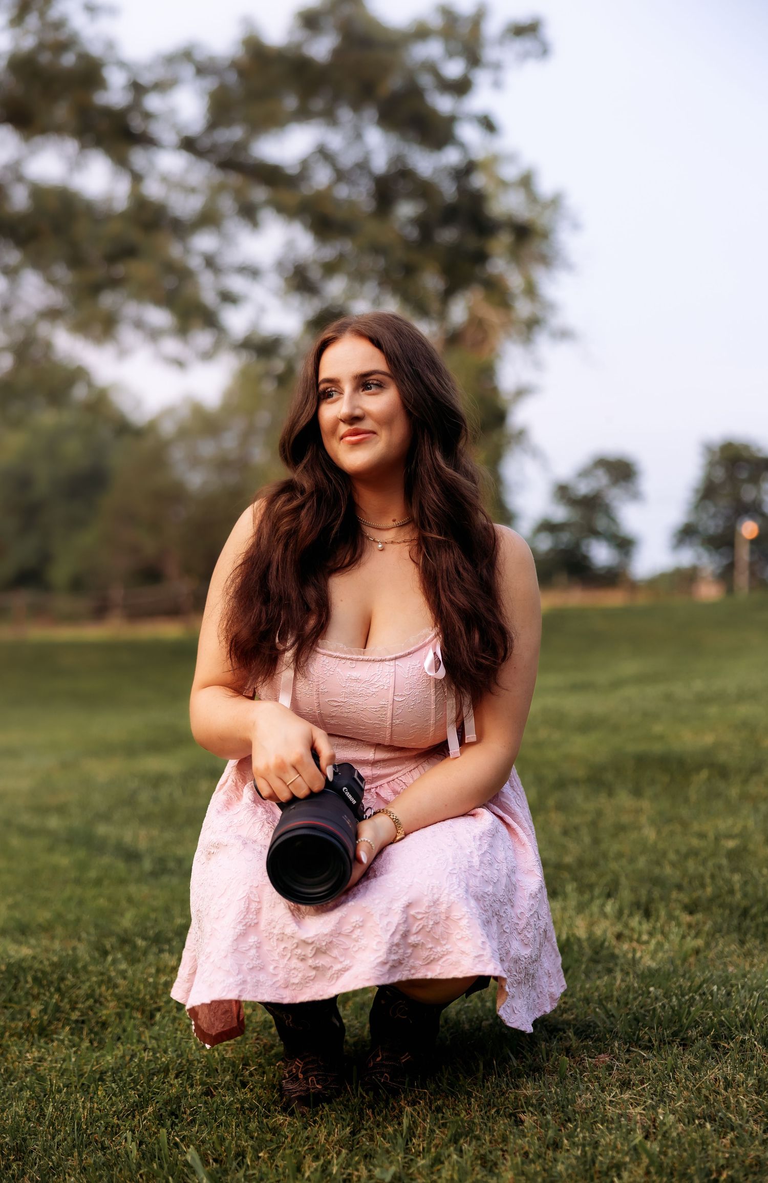 A photographer sits casually on grass holding camera equipment during an outdoor photoshoot.