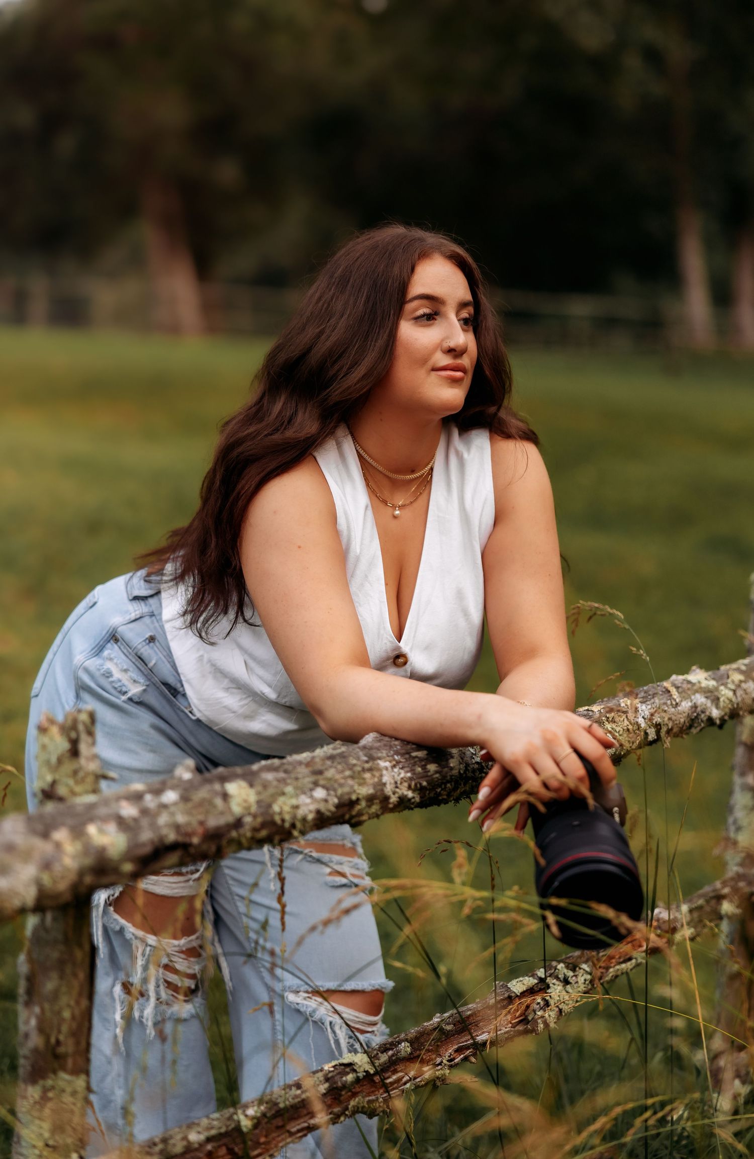 A photographer in casual denim attire leans on a rustic fence during golden hour.