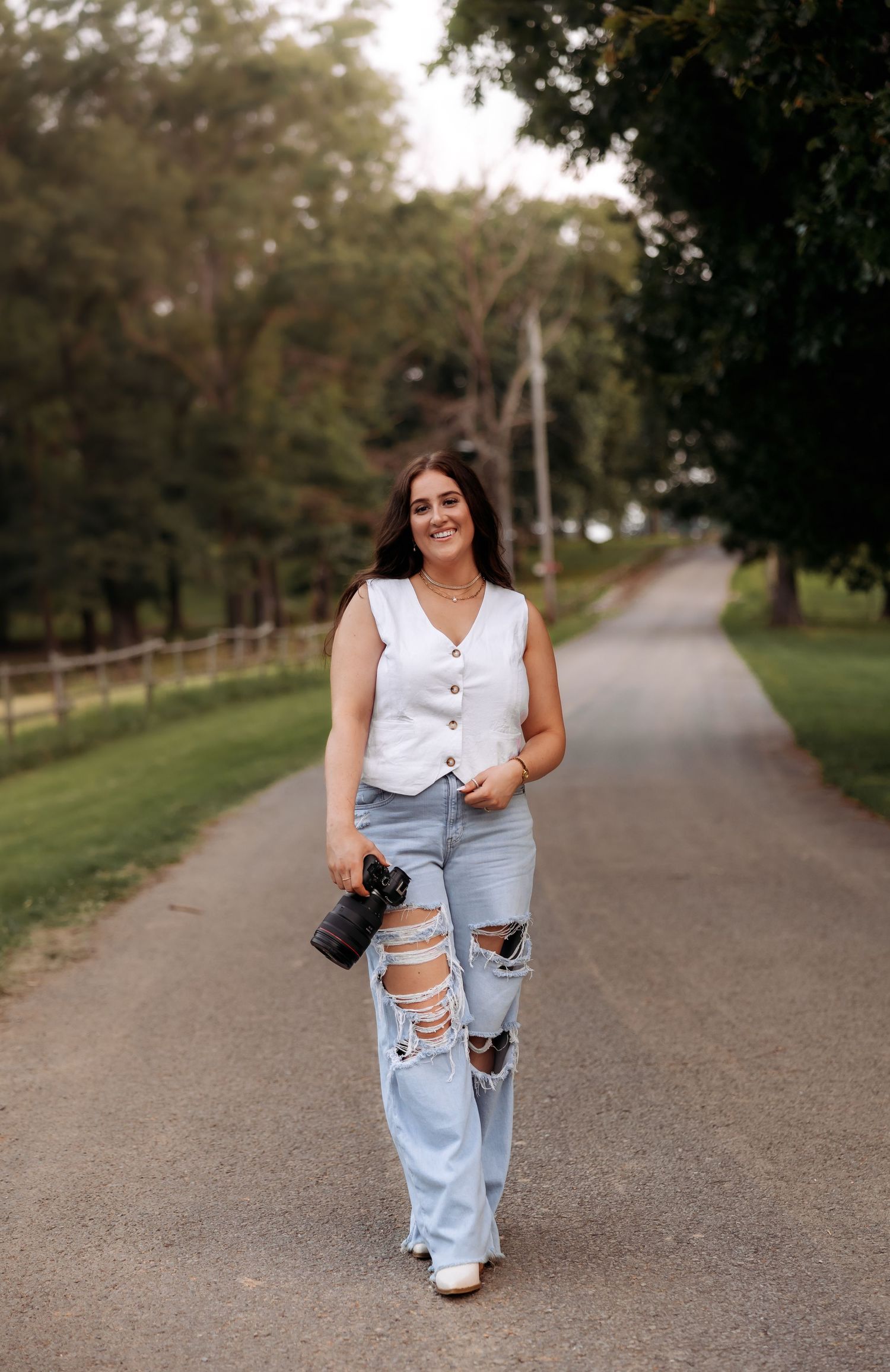 A photographer walks confidently down a tree-lined path carrying professional camera equipment.