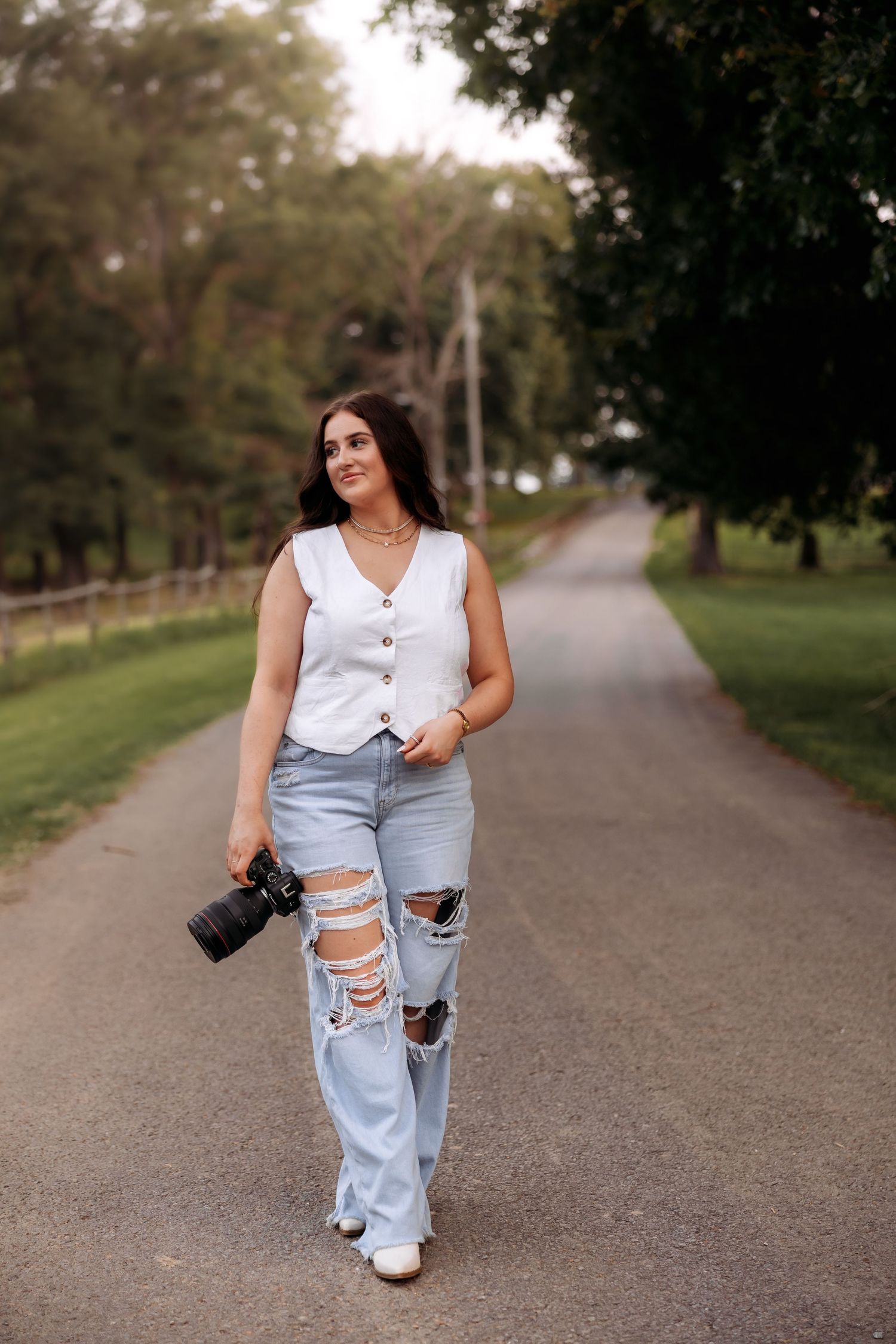 A photographer strolls along a scenic park path while holding camera gear.