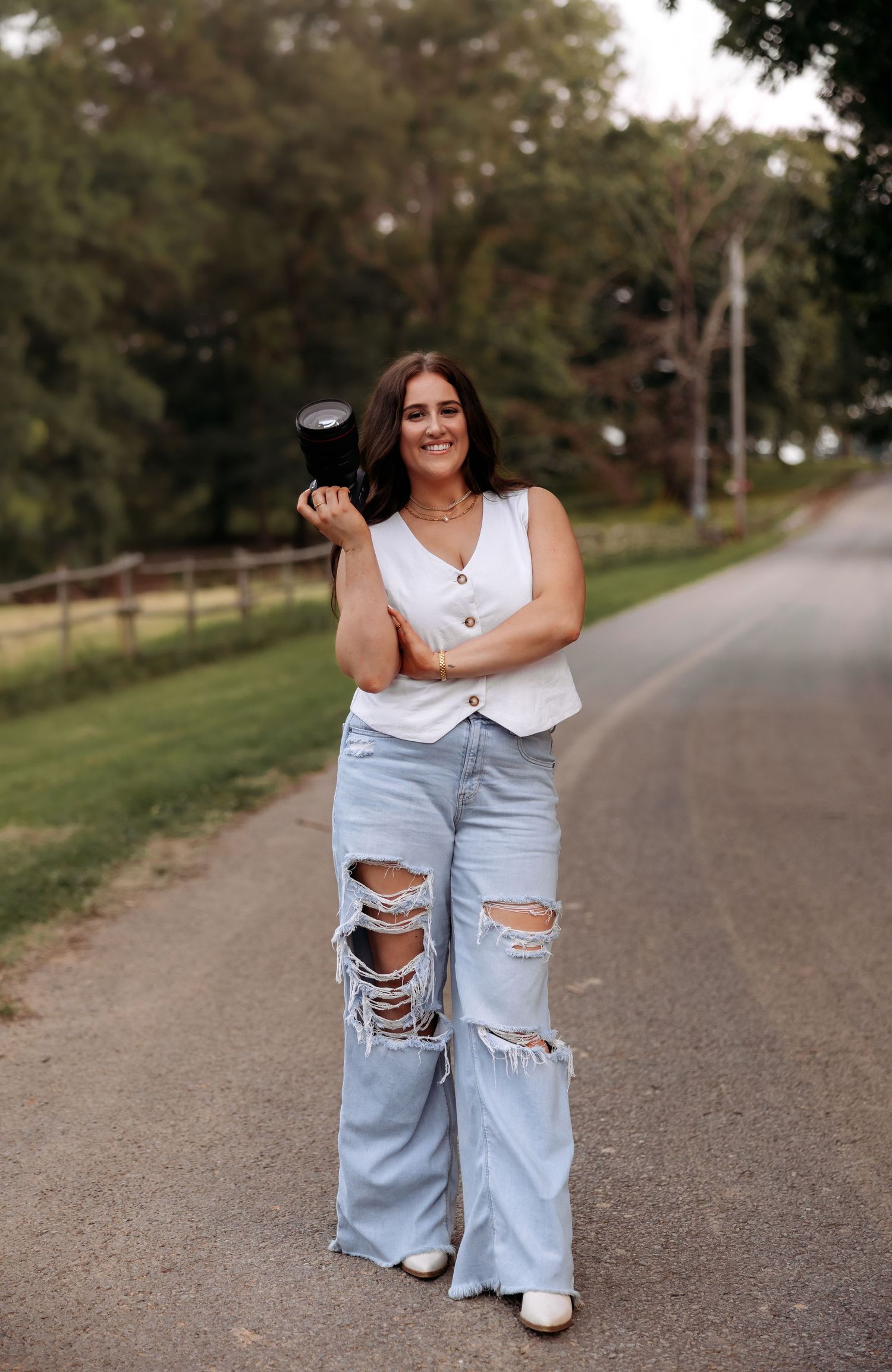 A person in ripped jeans and white top poses playfully on a rural path.