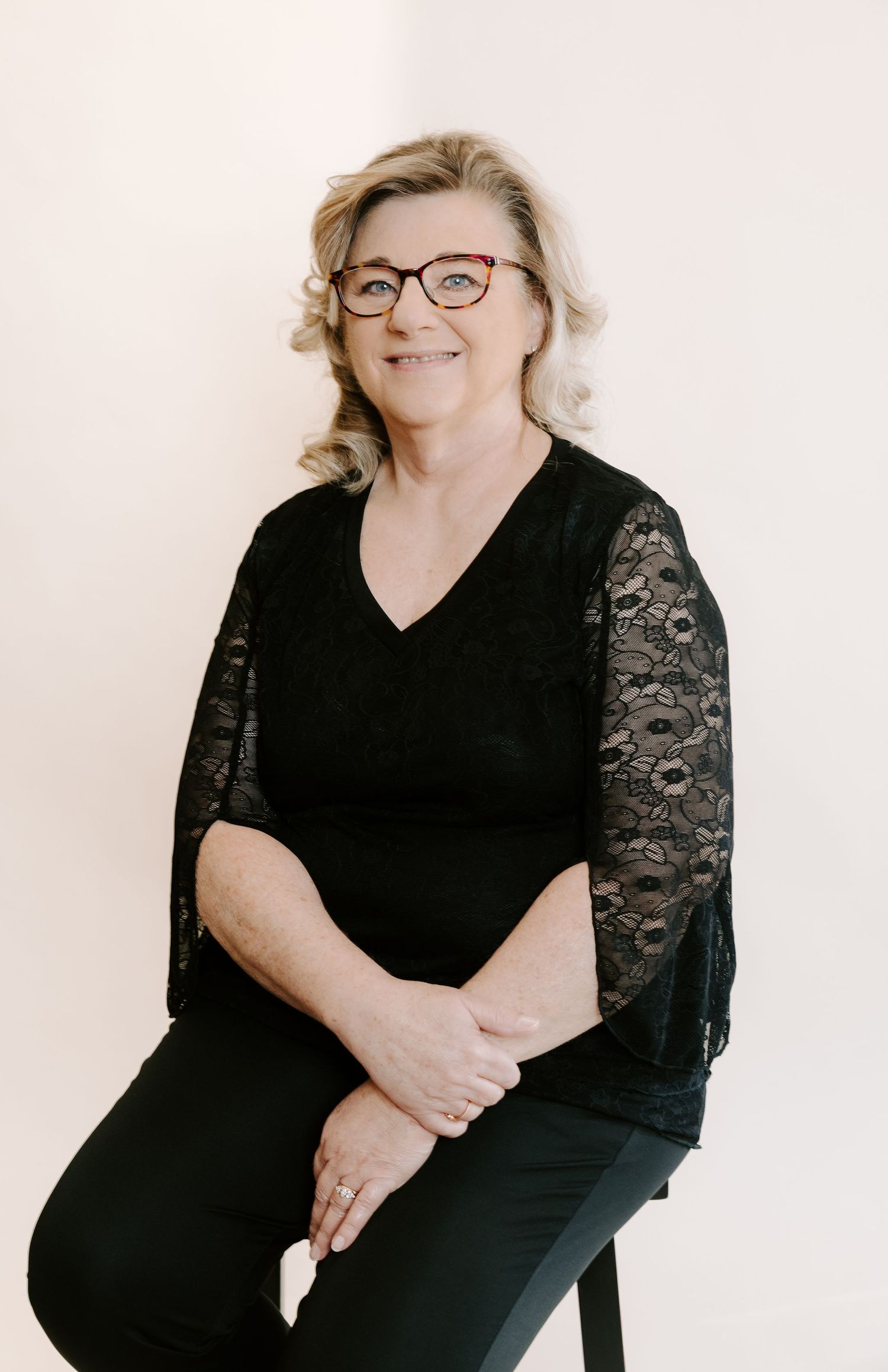Professional portrait of someone wearing glasses and a black lace-sleeved dress against a light background.