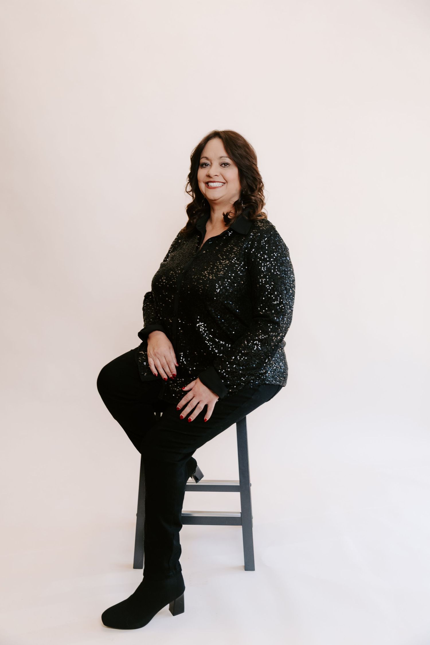 A series of four studio portraits showing someone in a sparkly black outfit posing on a stool against a white background.