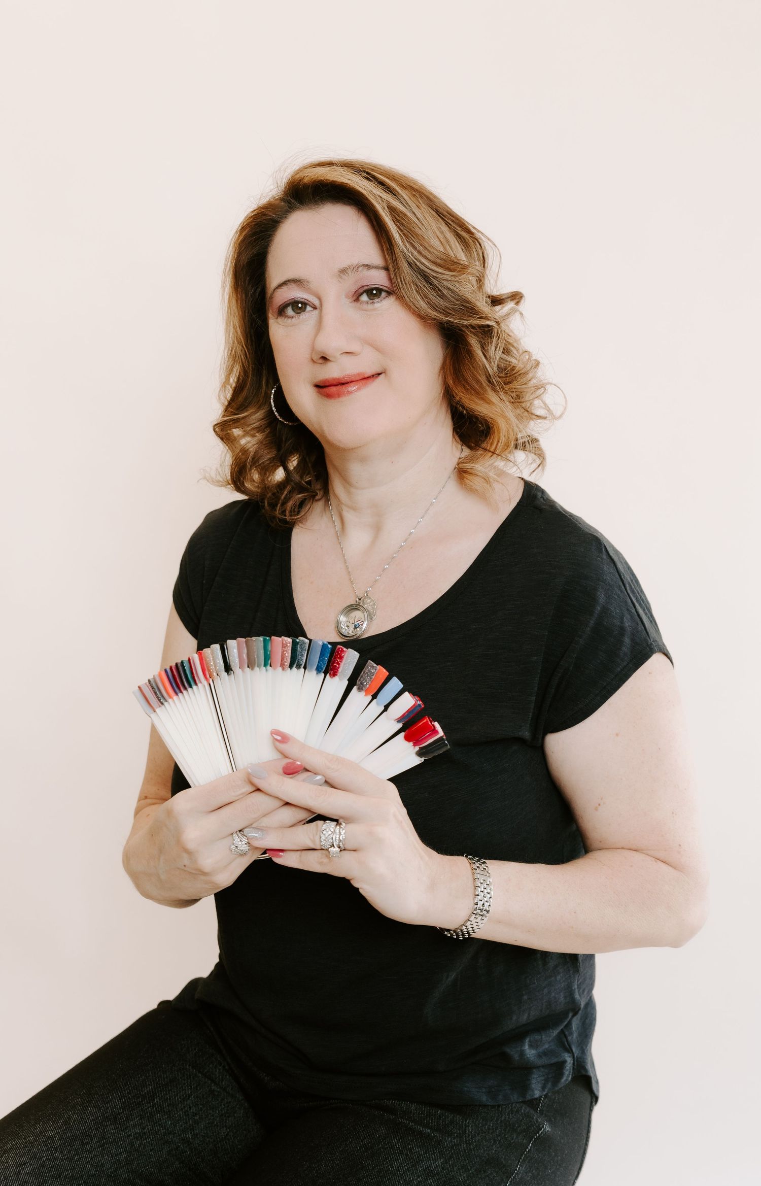 Professional holding nail polish color samples in a fan shape while wearing black attire against white background.