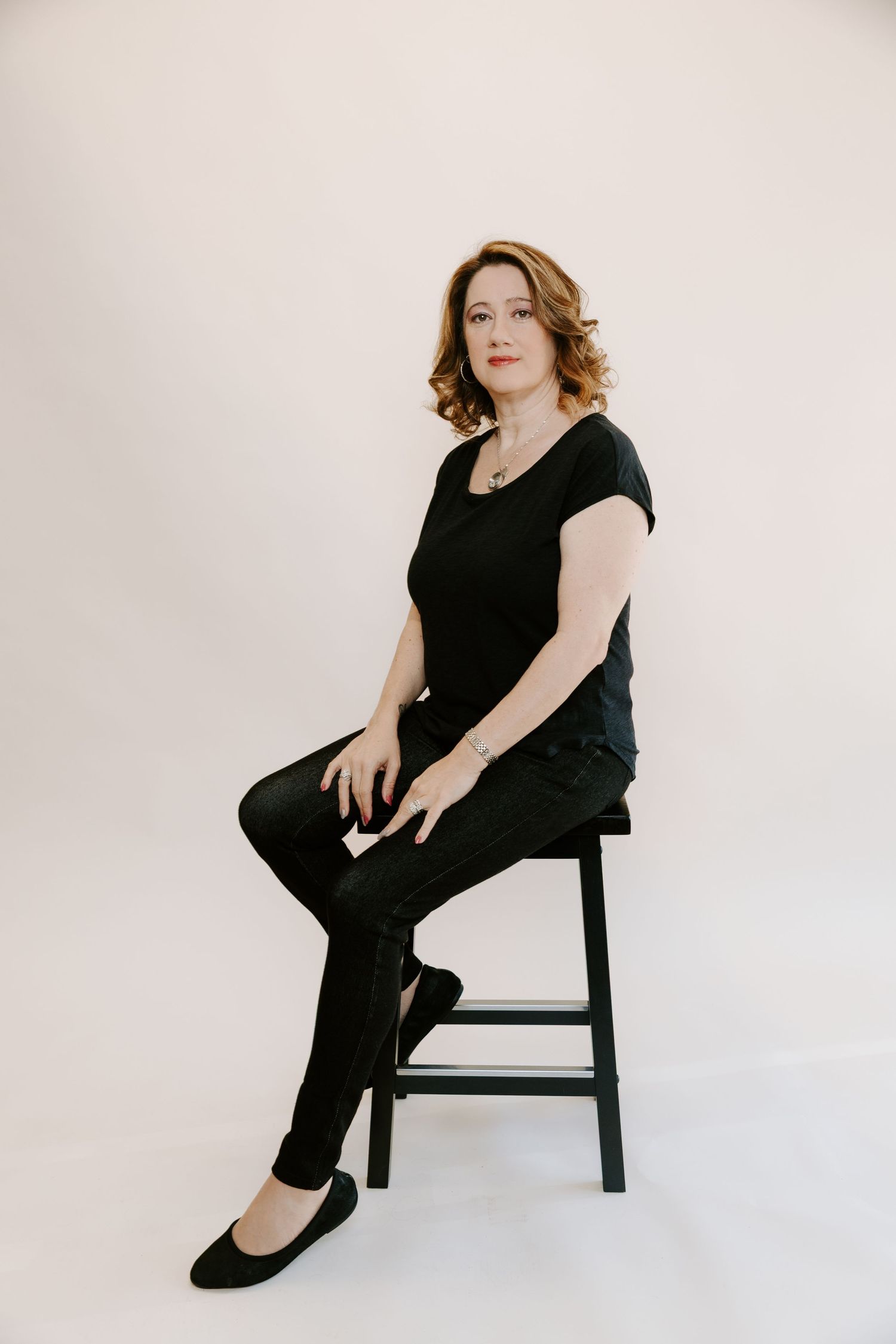 A figure in a black dress poses elegantly on a wooden chair against a white backdrop in a series of artistic portraits.
