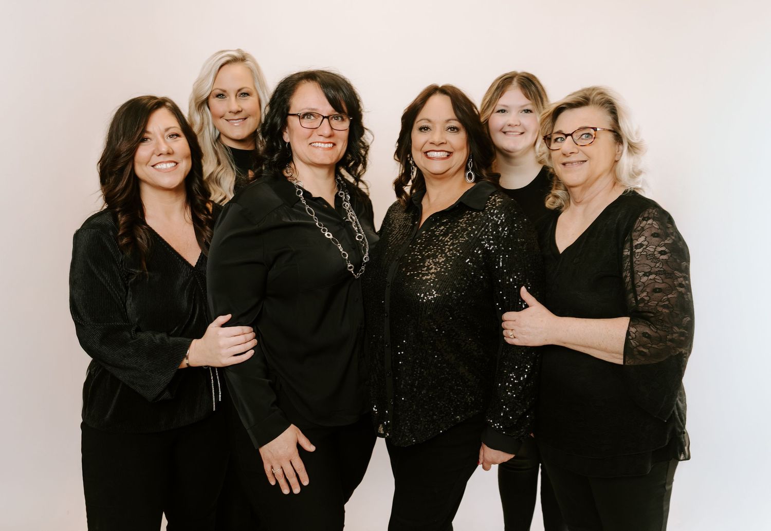 A group of women in black attire pose together for a series of professional studio photographs.
