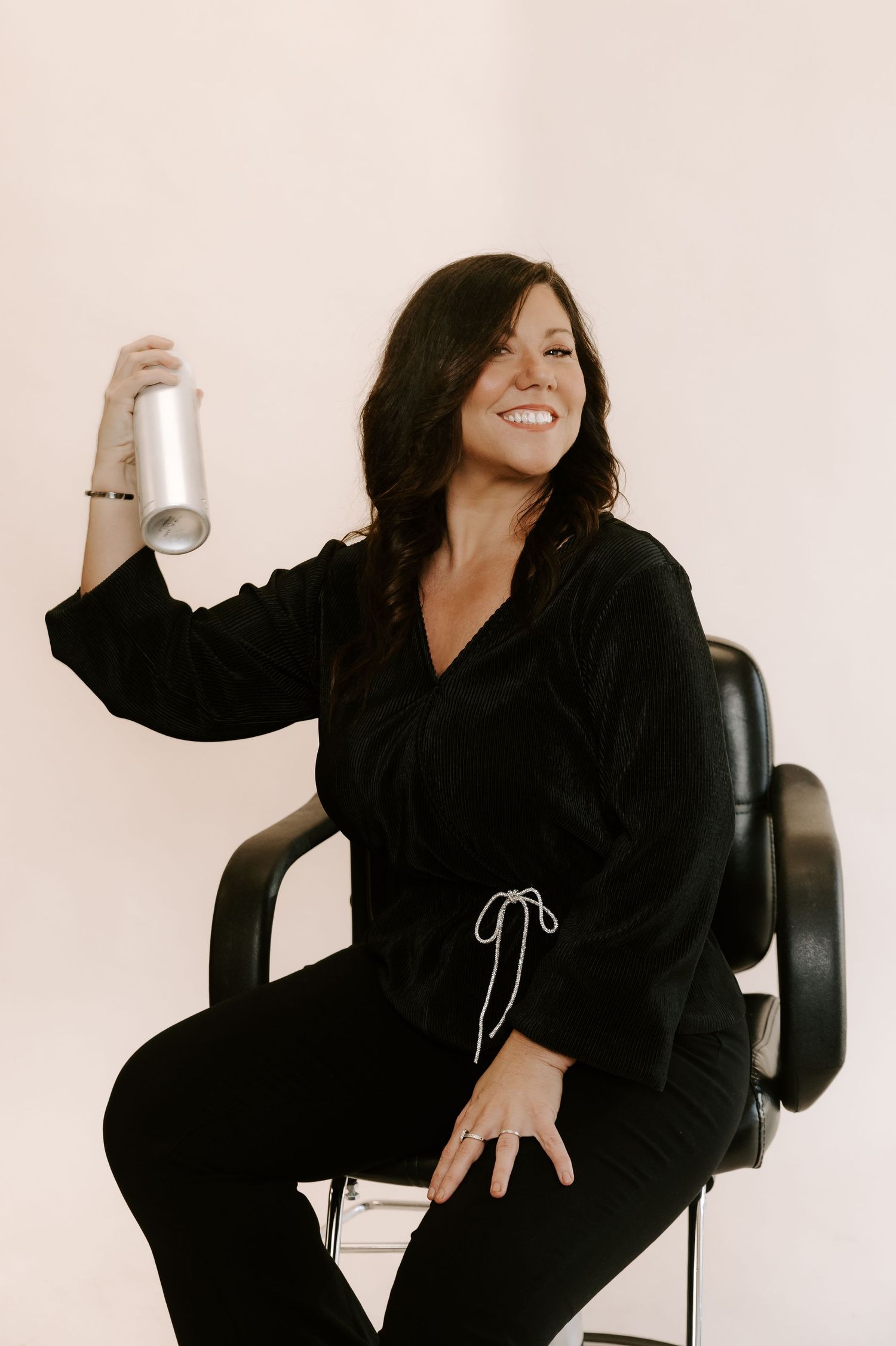 A person in a black loungewear set sits and poses playfully in a chair against a white background.