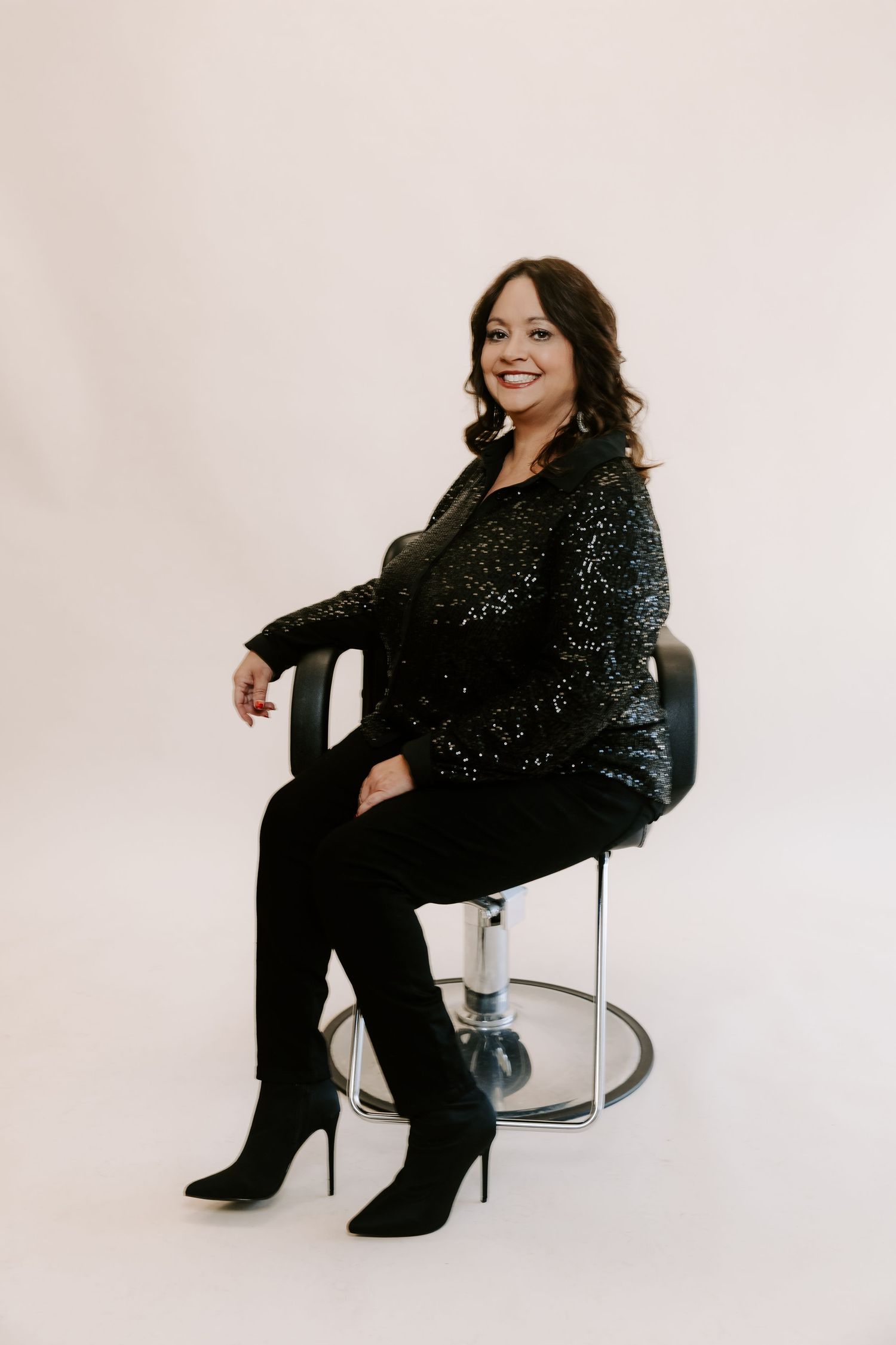 A person in a sparkling black outfit poses on a chair against a white backdrop in a series of studio photographs.