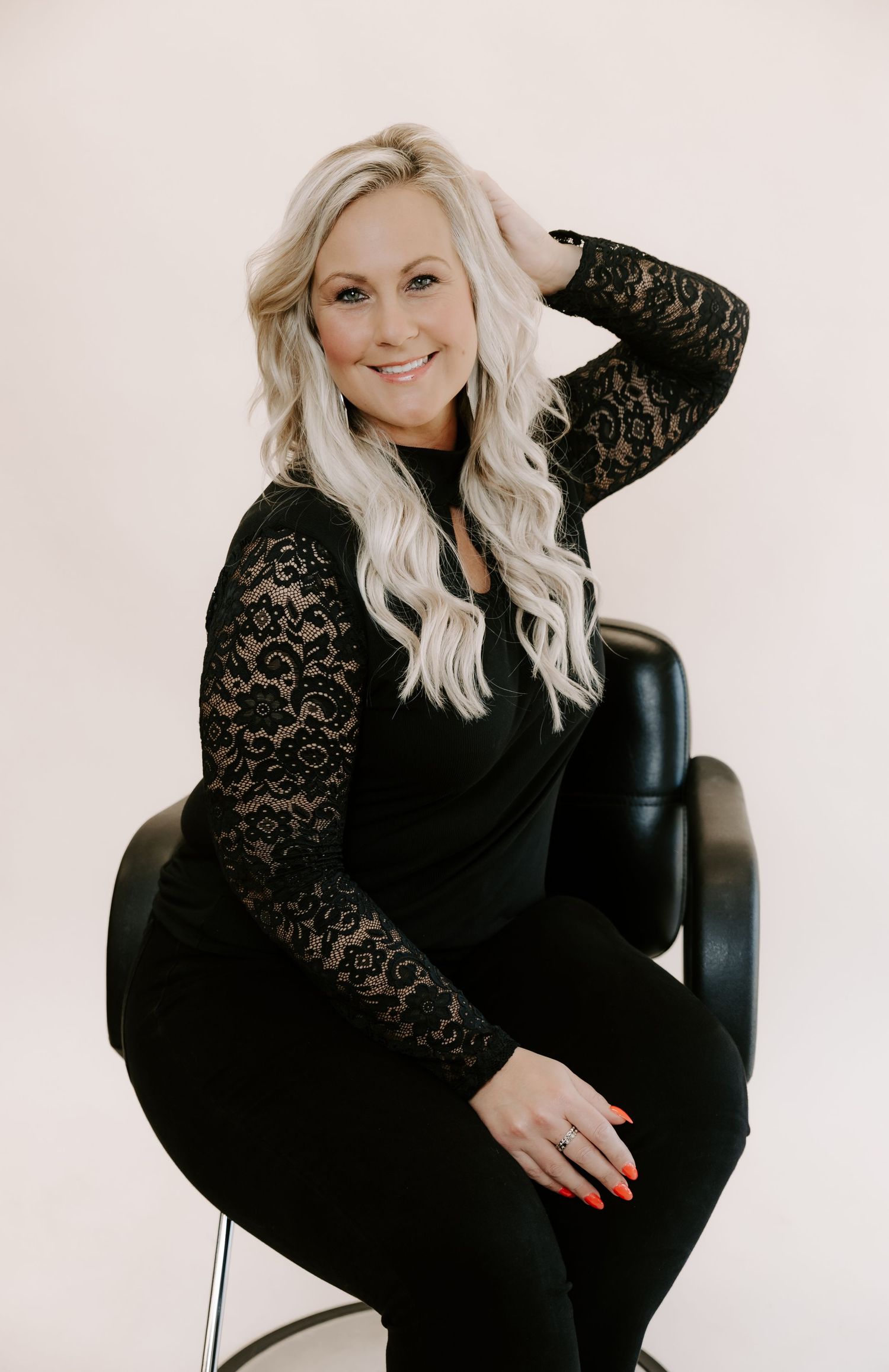 Professional studio portraits of a woman in black lace dress sitting on chair against light background.