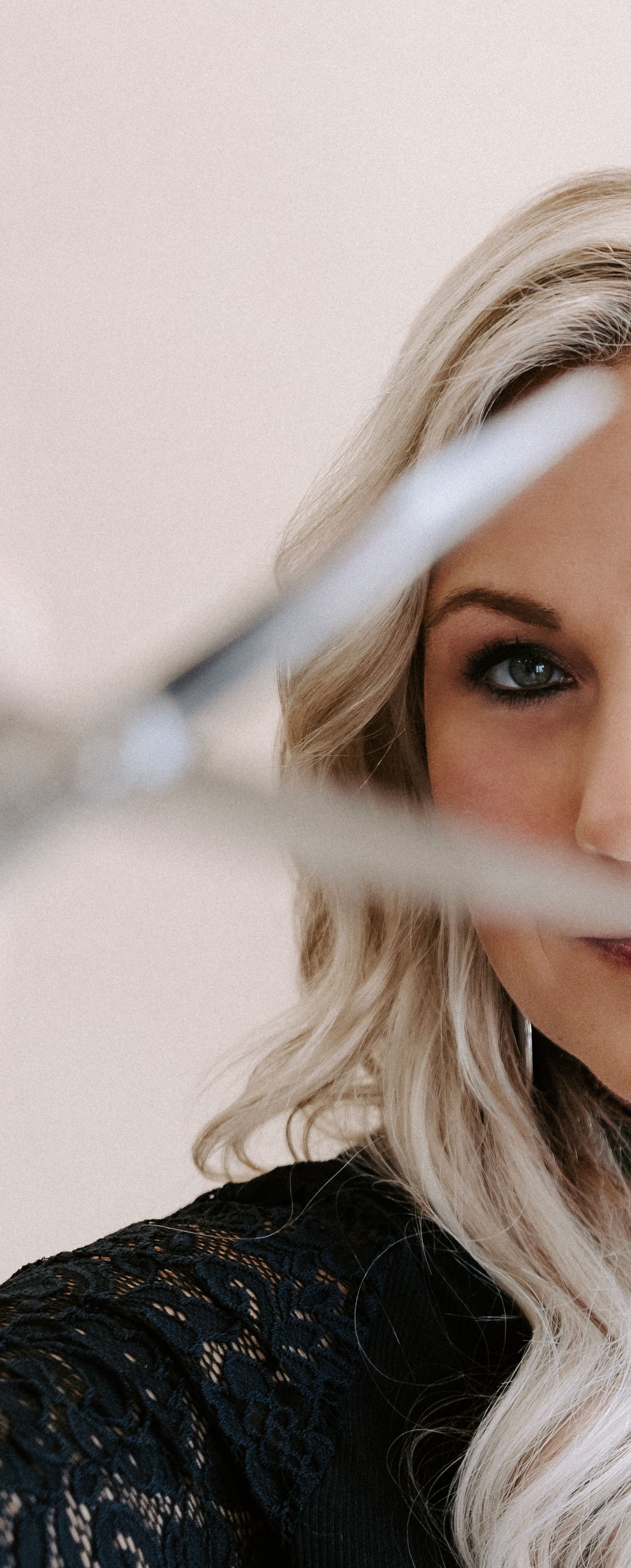 Artistic portrait of a woman with platinum blonde hair and smokey eye makeup wearing black lace, partially obscured by a blurred line.