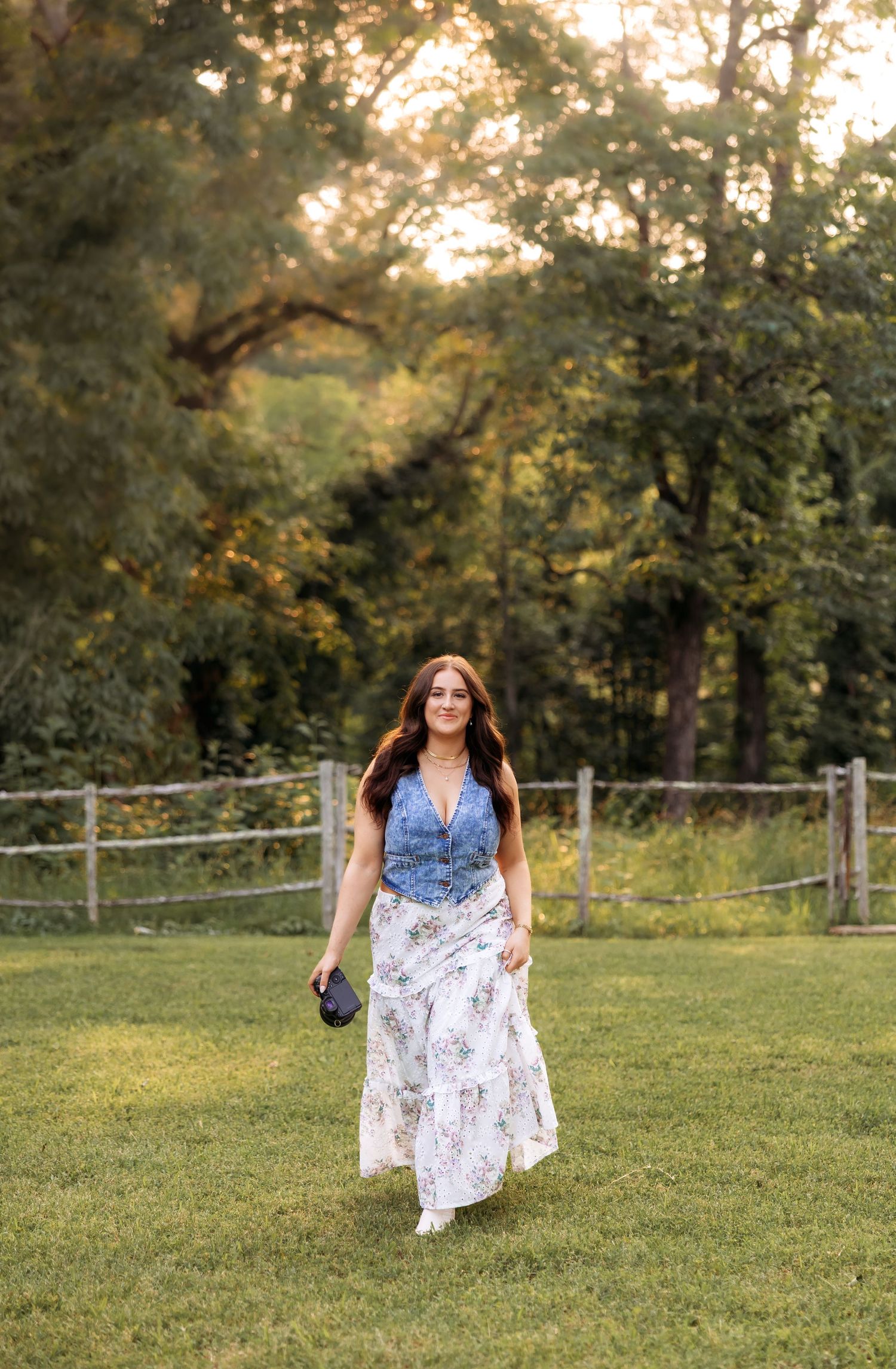 A photographer walks through a grassy field at sunset holding camera equipment.