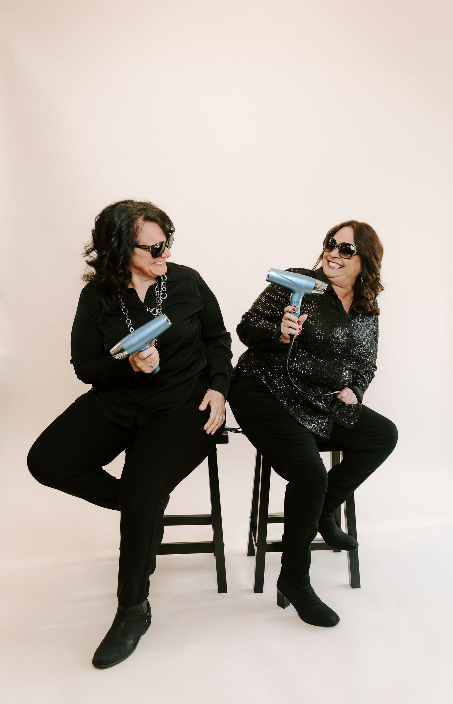 A sequence of photos showing two people in black outfits sitting on chairs and interacting playfully against a white backdrop.