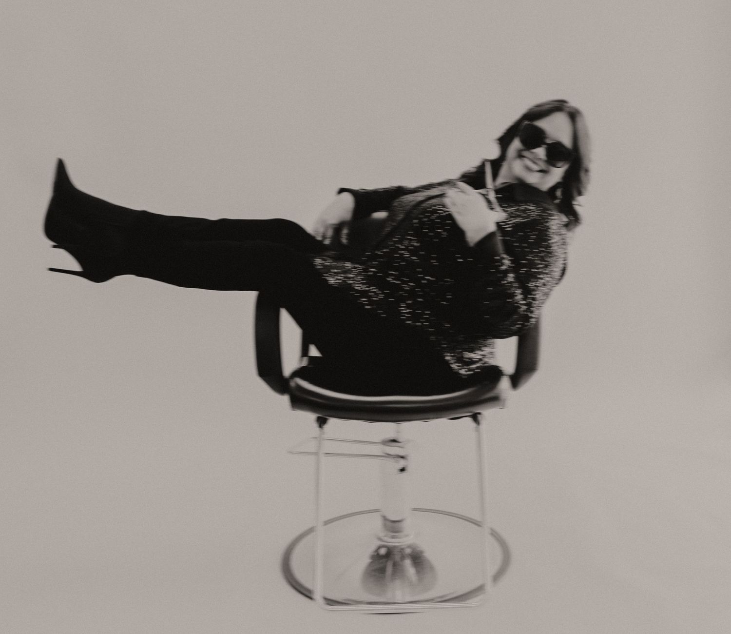A black cat lounges gracefully on a clear glass pedestal in a series of artistic black and white photographs.