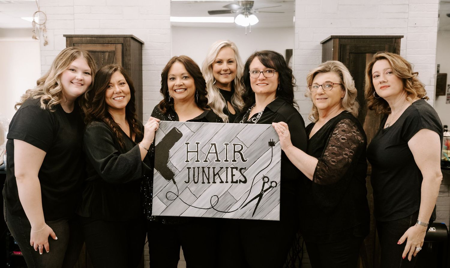 A group of women in black outfits smiling and posing together in a salon setting.