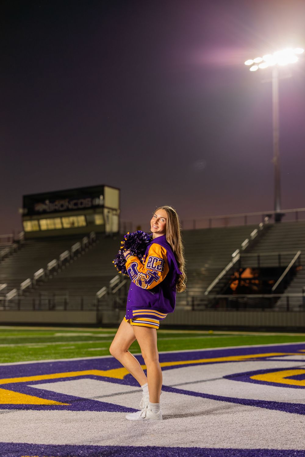 Cheerleader performs routine on illuminated football field at night.
