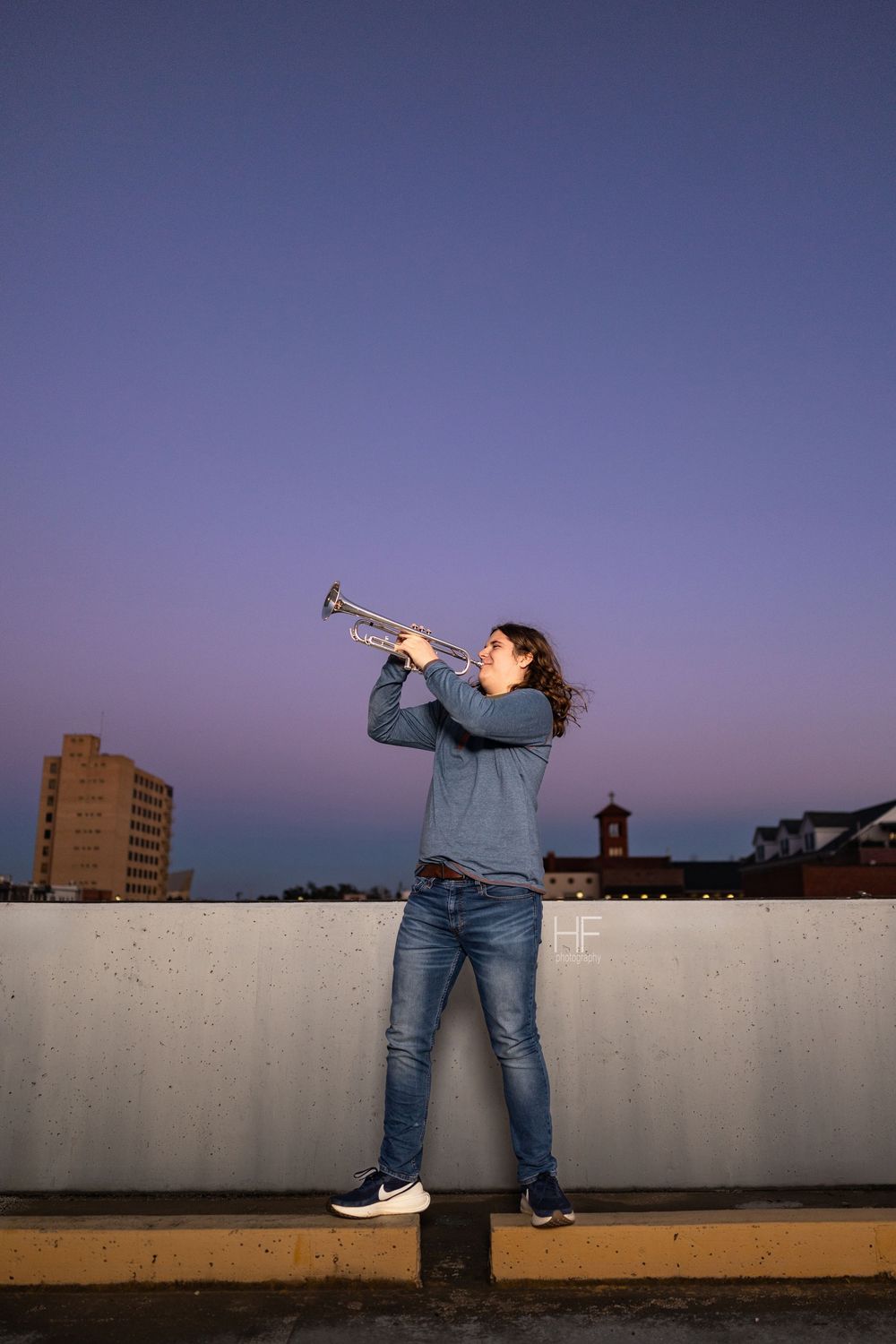 Silhouetted figure playing trumpet against twilight sky on urban rooftop.