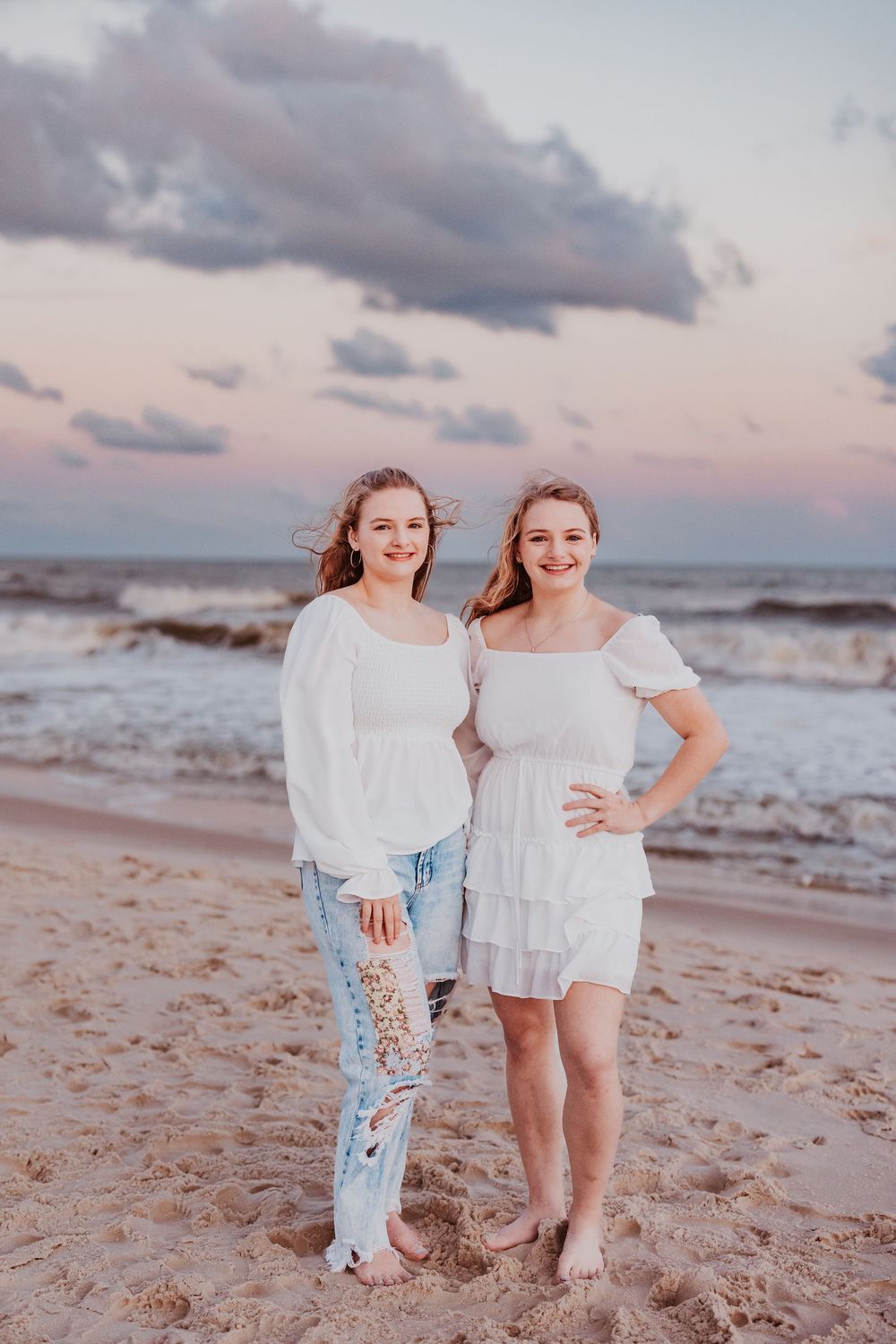 Two people in white outfits share happy moment on beach at sunset.