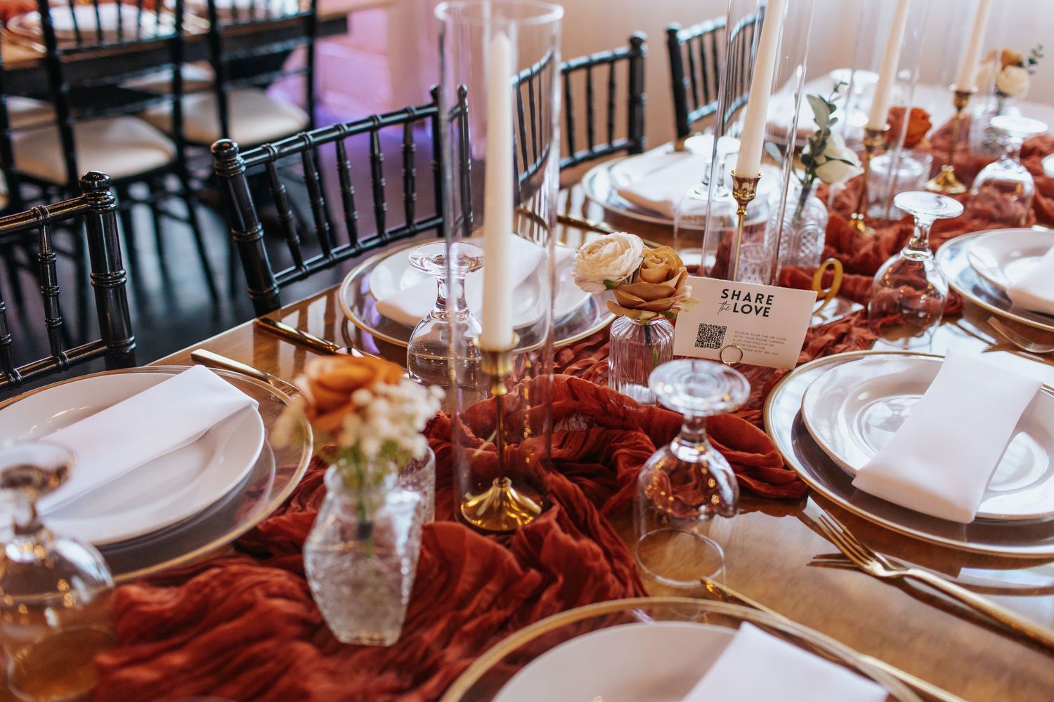 Elegant wedding reception table setting with red velvet linens and tall white candles.