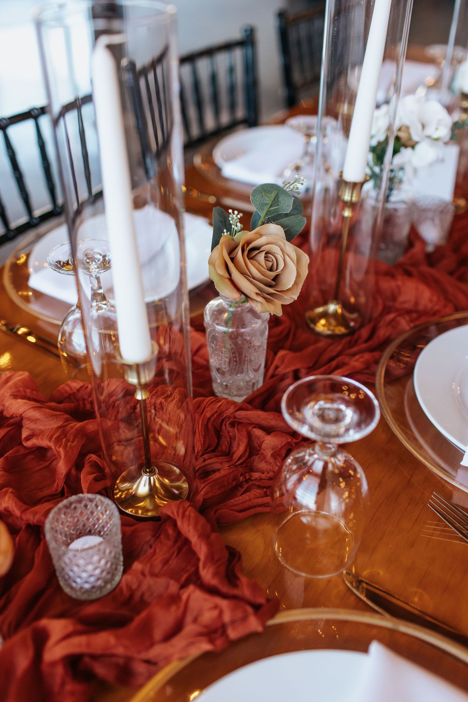 Romantic table setting with white candles, gold chargers and a single champagne rose on red fabric.
