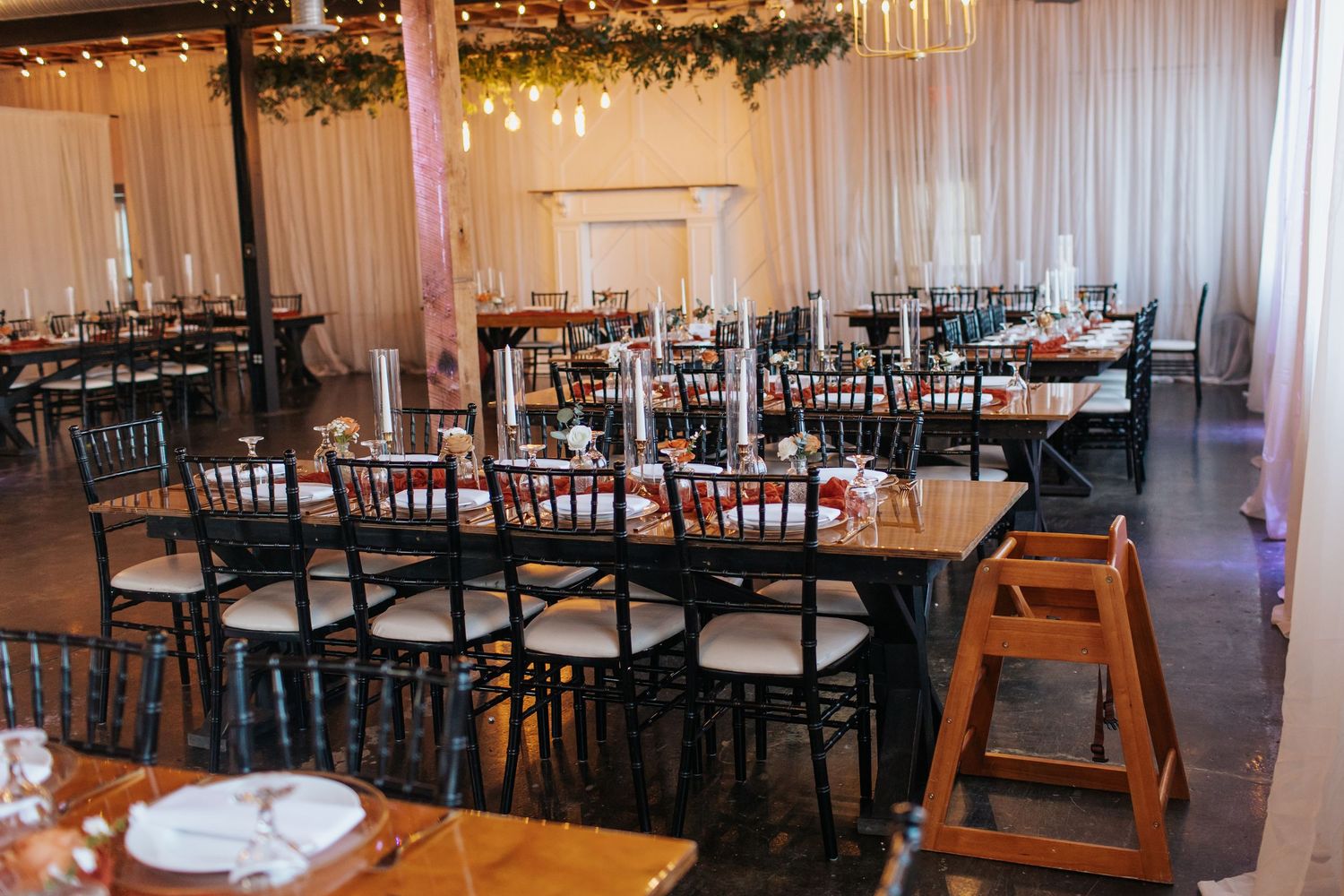 Wedding reception venue with black chiavari chairs and draped white fabric walls.