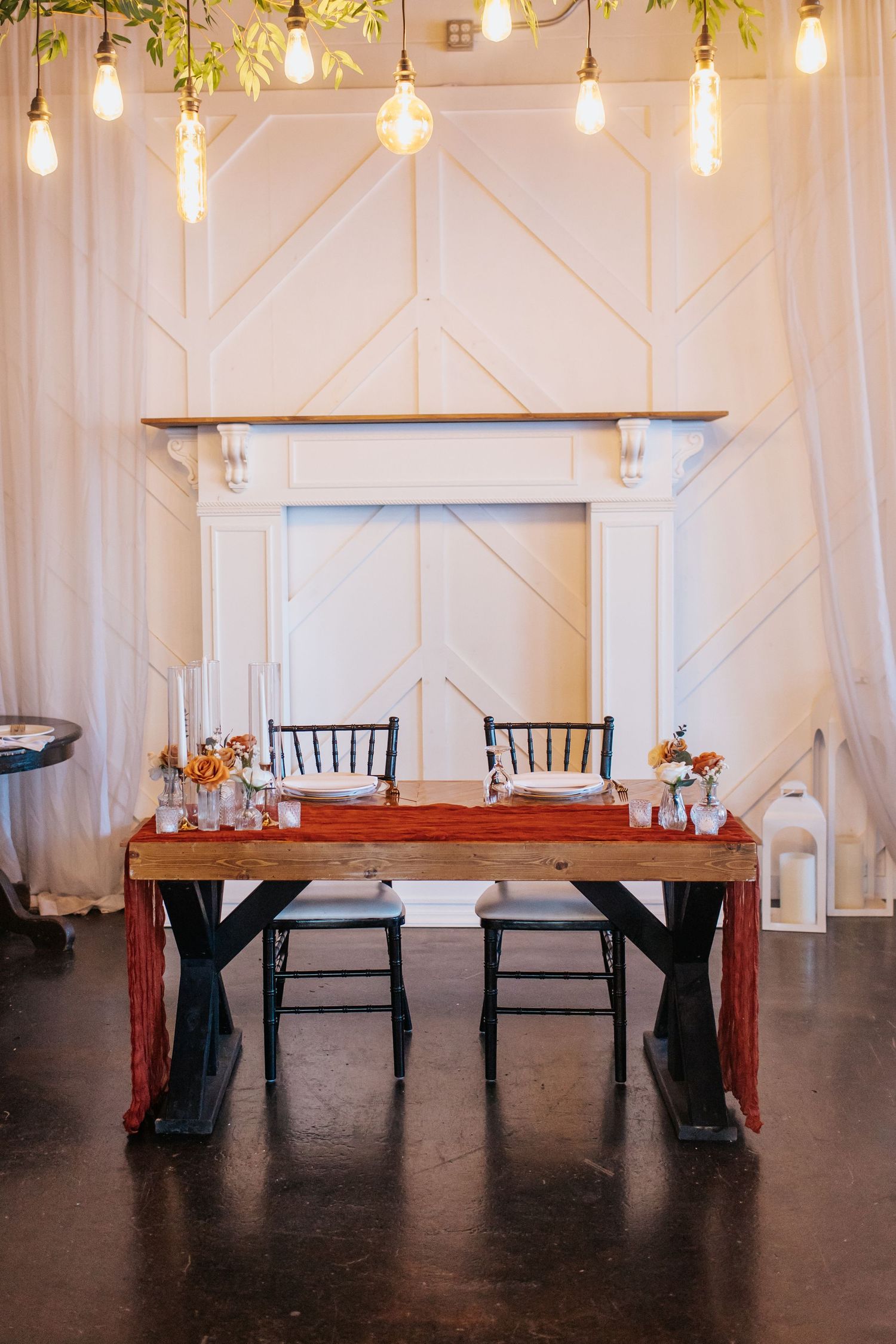 Modern wedding sweetheart table setup with hanging lights and geometric wall paneling.
