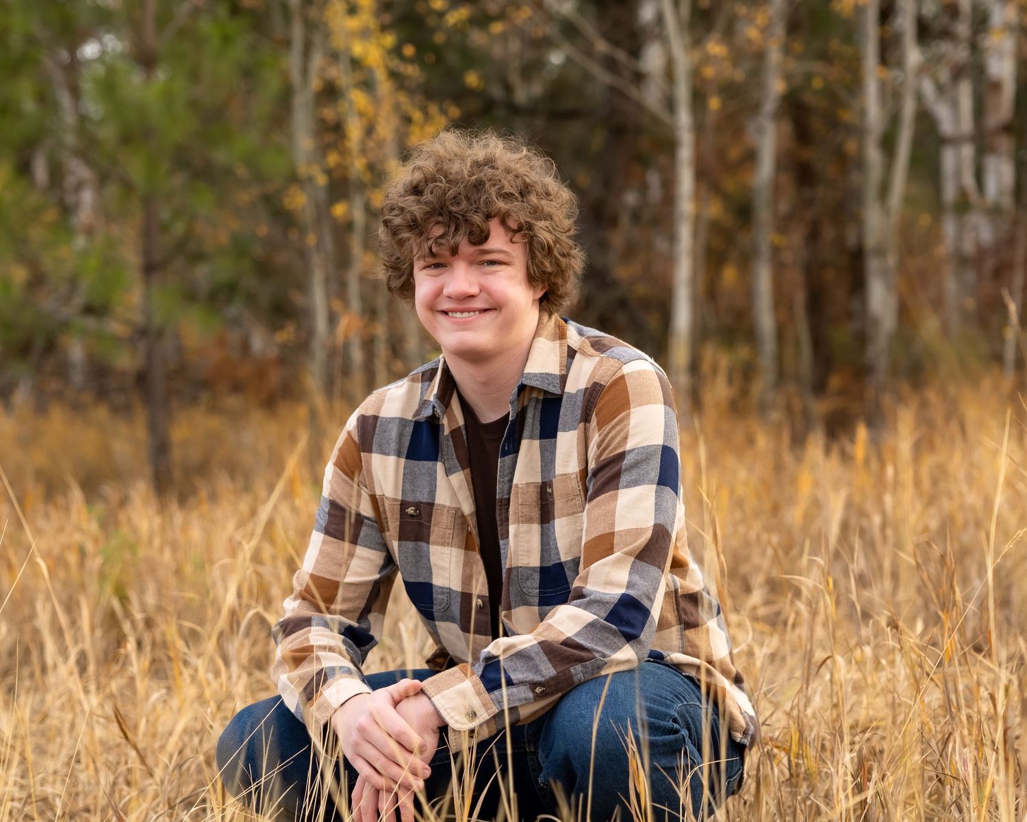 A person in a plaid flannel shirt sits in tall autumn grass during a golden hour outdoor photo session.