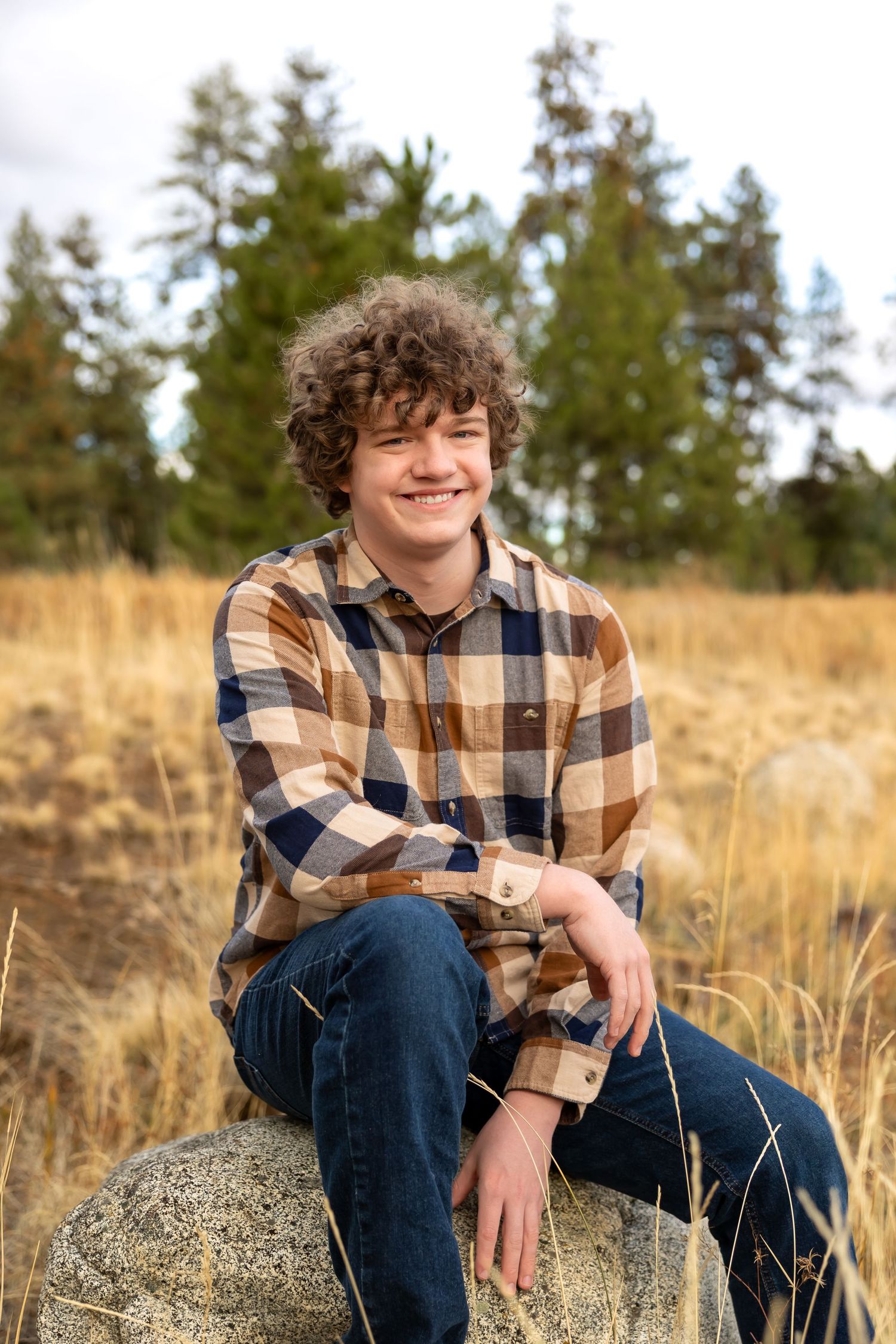 A plaid flannel shirt-wearing figure sits casually on a large rock in a grassy field during autumn.